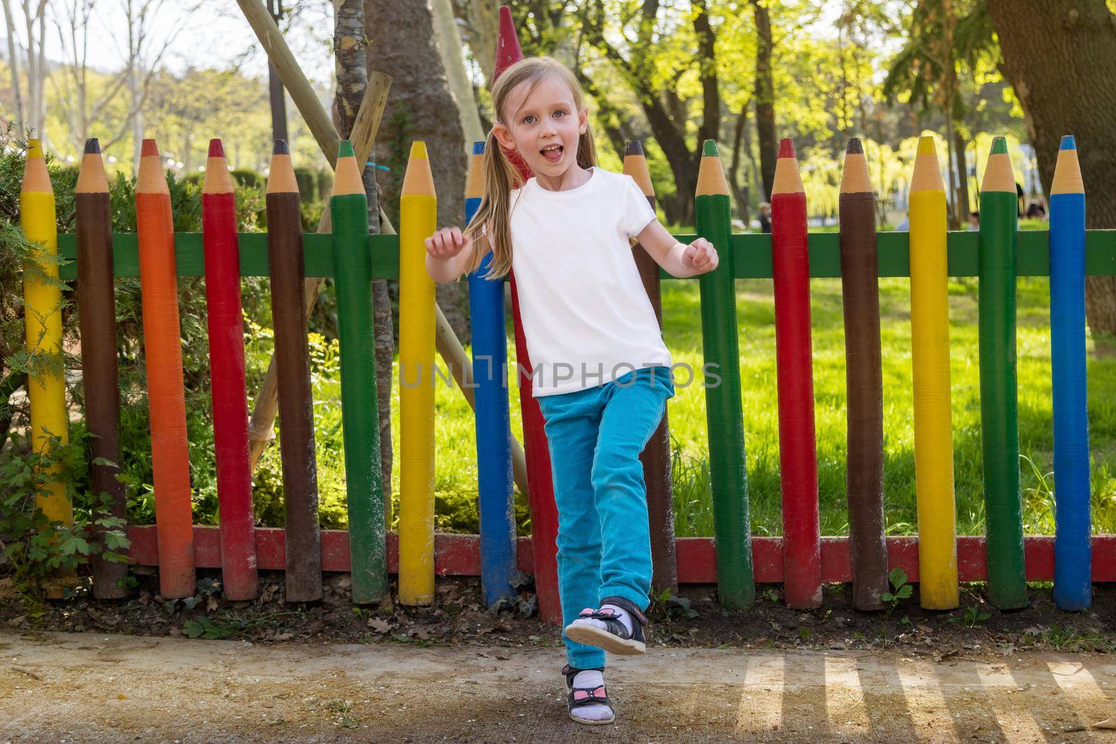 Mock-up of children's summer clothes, sportswear, uniforms. Little girl in a white t-shirt with space for an image or logo. park or outside. Children's bright background, on a school theme.