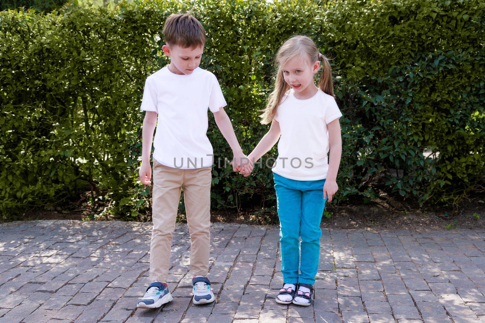 mockup white t-shirt. boy, girl holding hands, walking in the park on summer day by Ramanouskaya
