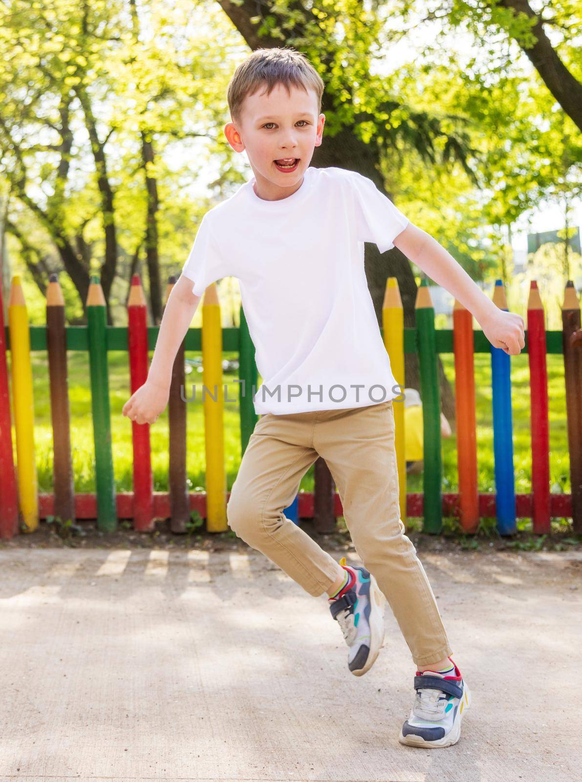 Mockup, template for children's clothing, sportswear, uniforms. A small, cheerful boy laughs and dances in the park. The child is wearing a white T-shirt with an empty space for design