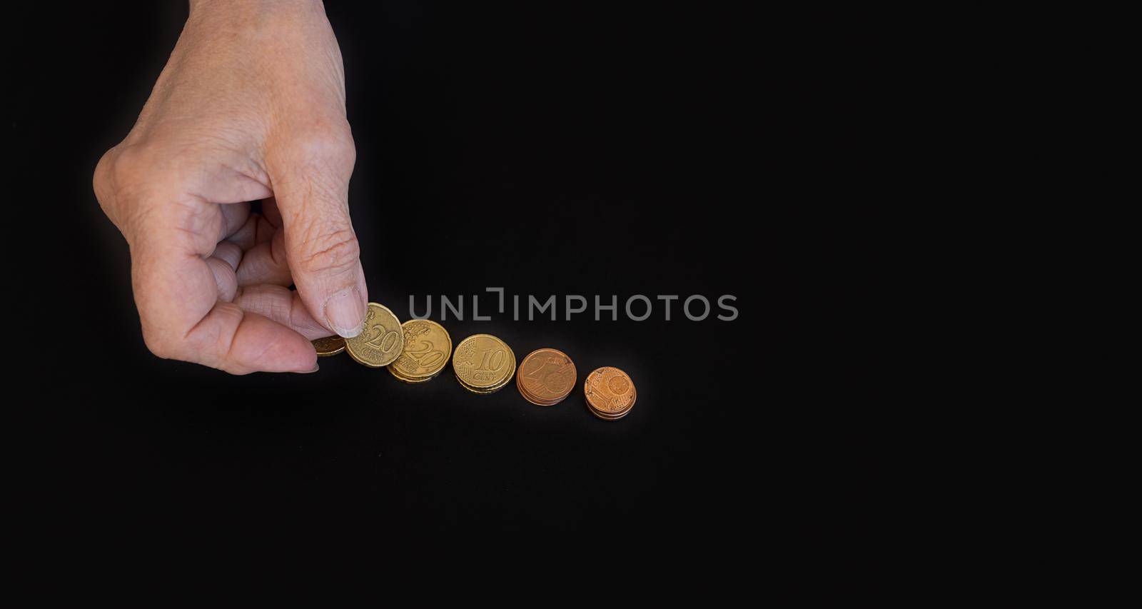 close-up, the hands of the old woman put the coins in piles. Poster on black background with copy paste for text. The concept of poverty, small benefits for the elderly, financial crisis, low pensions
