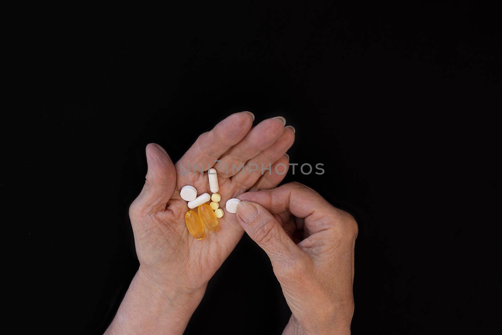 An elderly woman chooses which pill to take, hands on a black background by Ramanouskaya