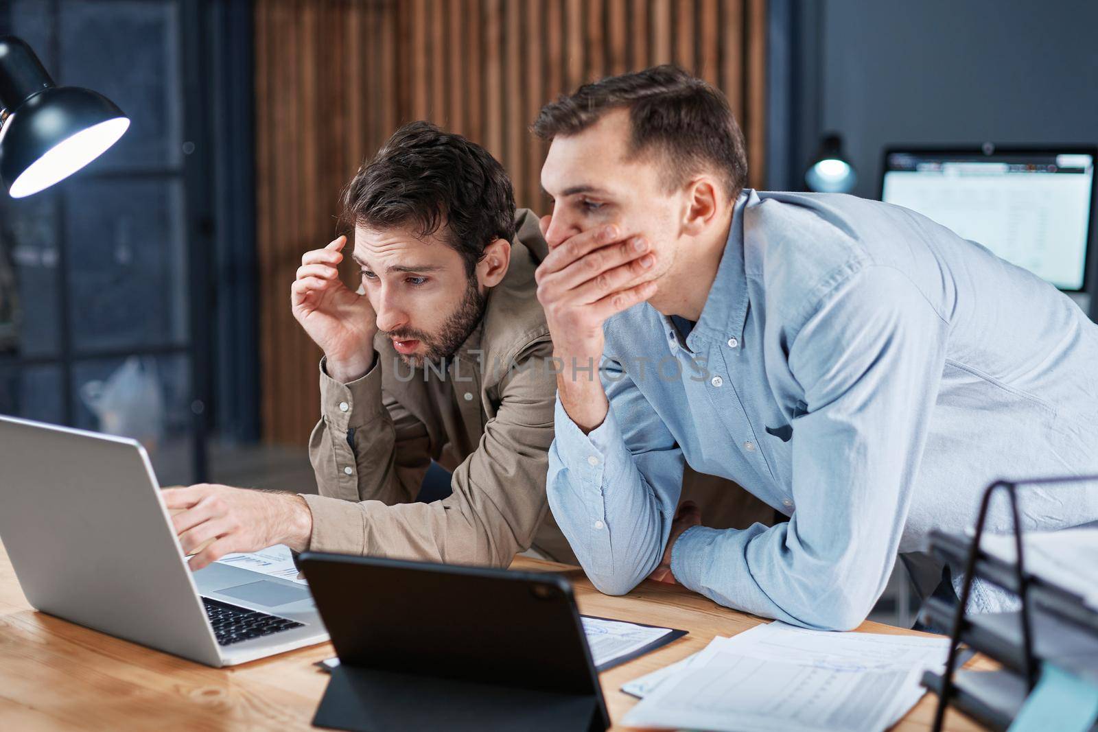 two tired employees working with financial documents until late at night . by SmartPhotoLab