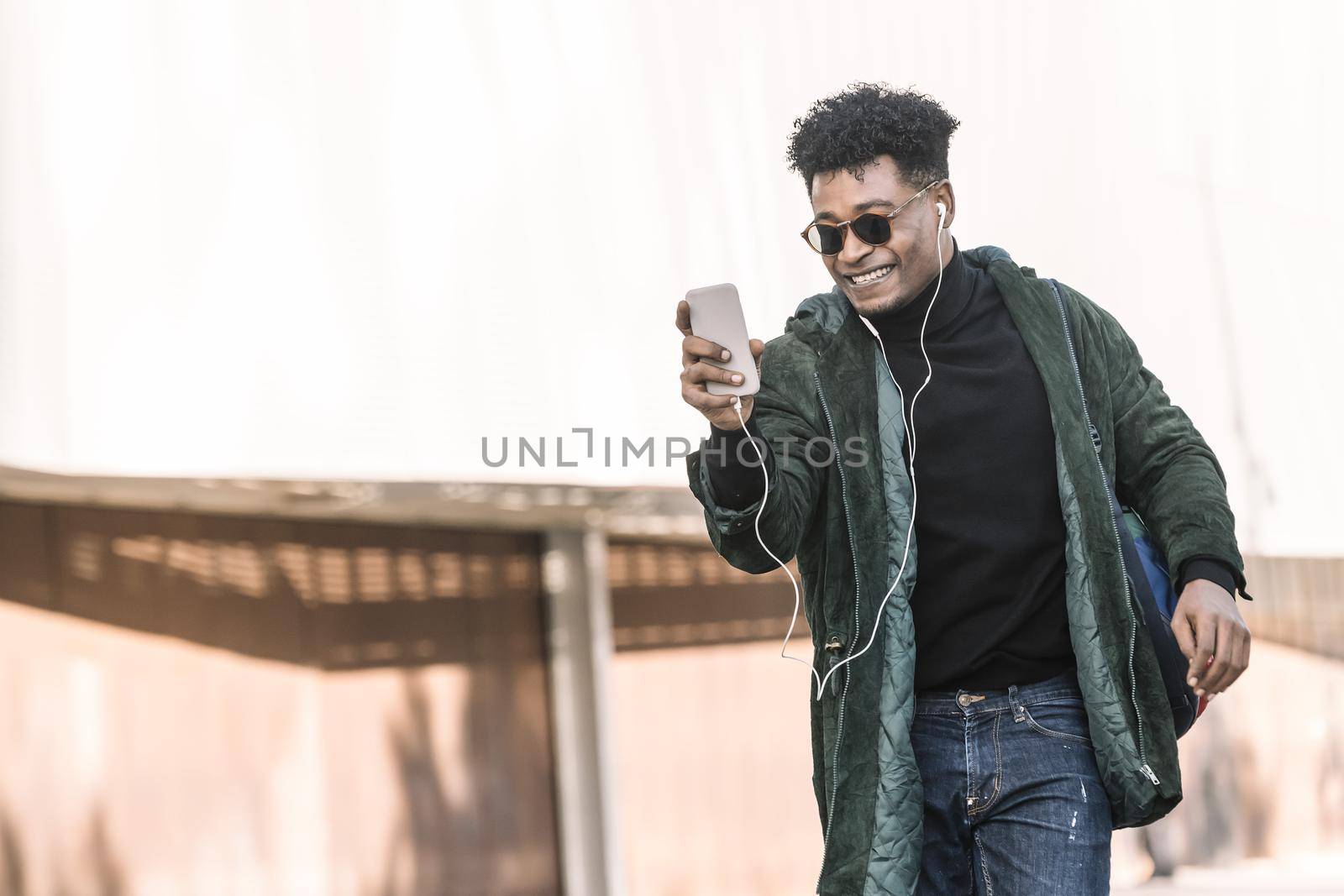 black young man with earphones making a video call with a mobile phone, technology and lifestyle concept using internet electronic device outdoors