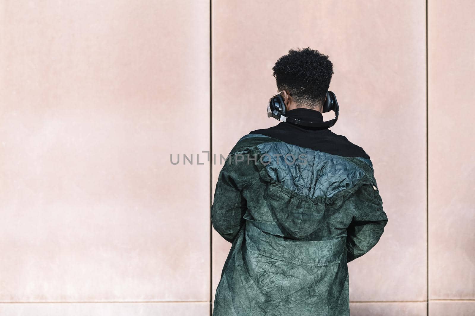 back view of a black man with headphones to listen music in front of a wall, technology and lifestyle concept