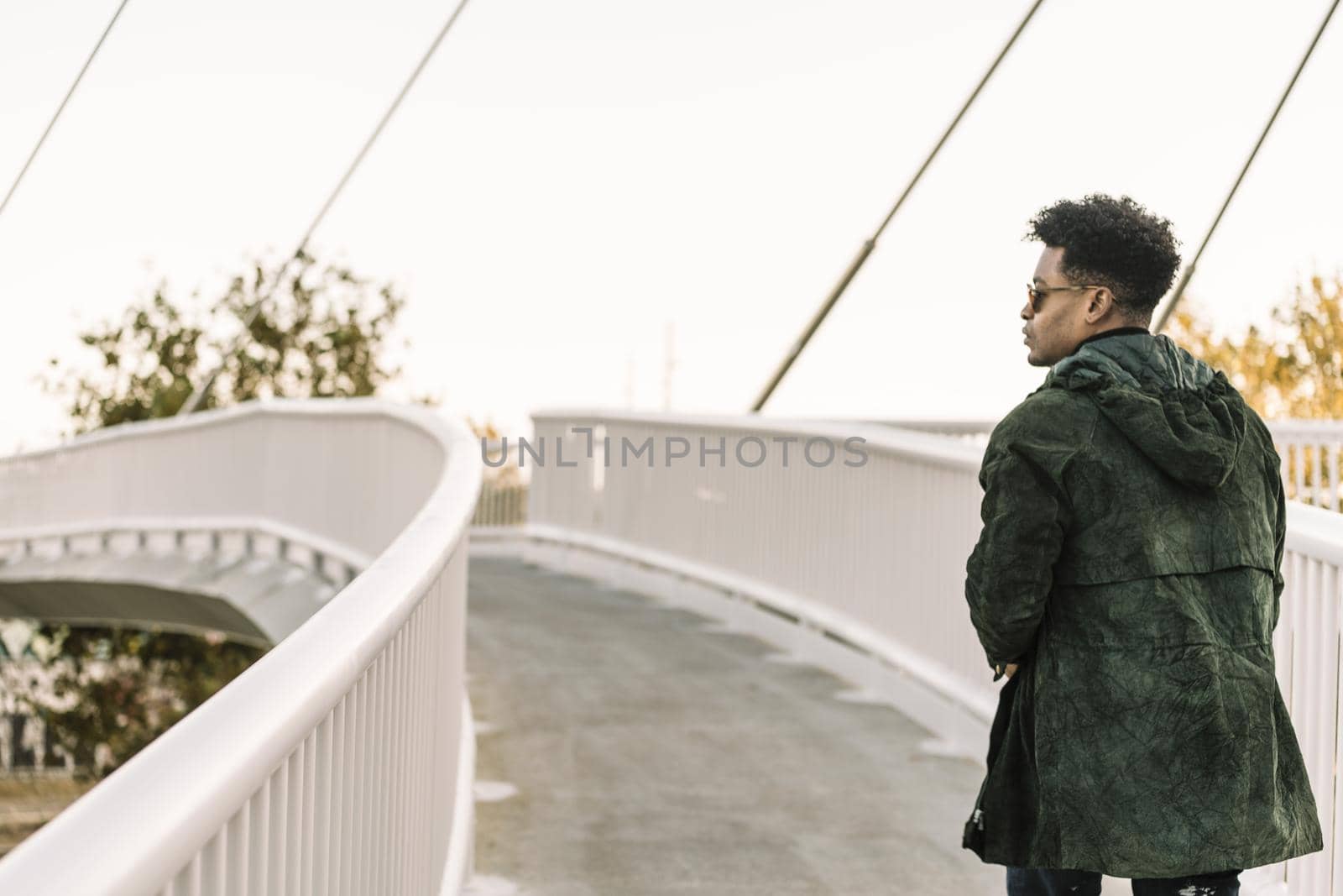 view from behind attractive young black african man with cool casual wear and sunglasses walking on a modern bridge in the city, lifestyle concept