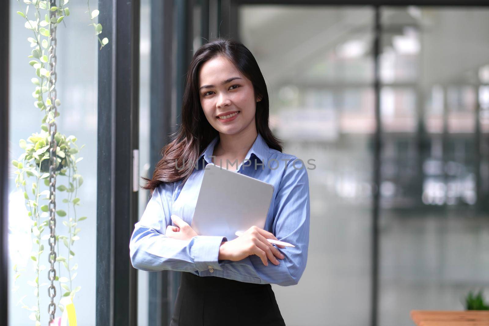 Asian businesswoman looking at camera with crossed arms holding a laptop and tablet at work Concepts of business accounting, planning, analytical and reporting documents..