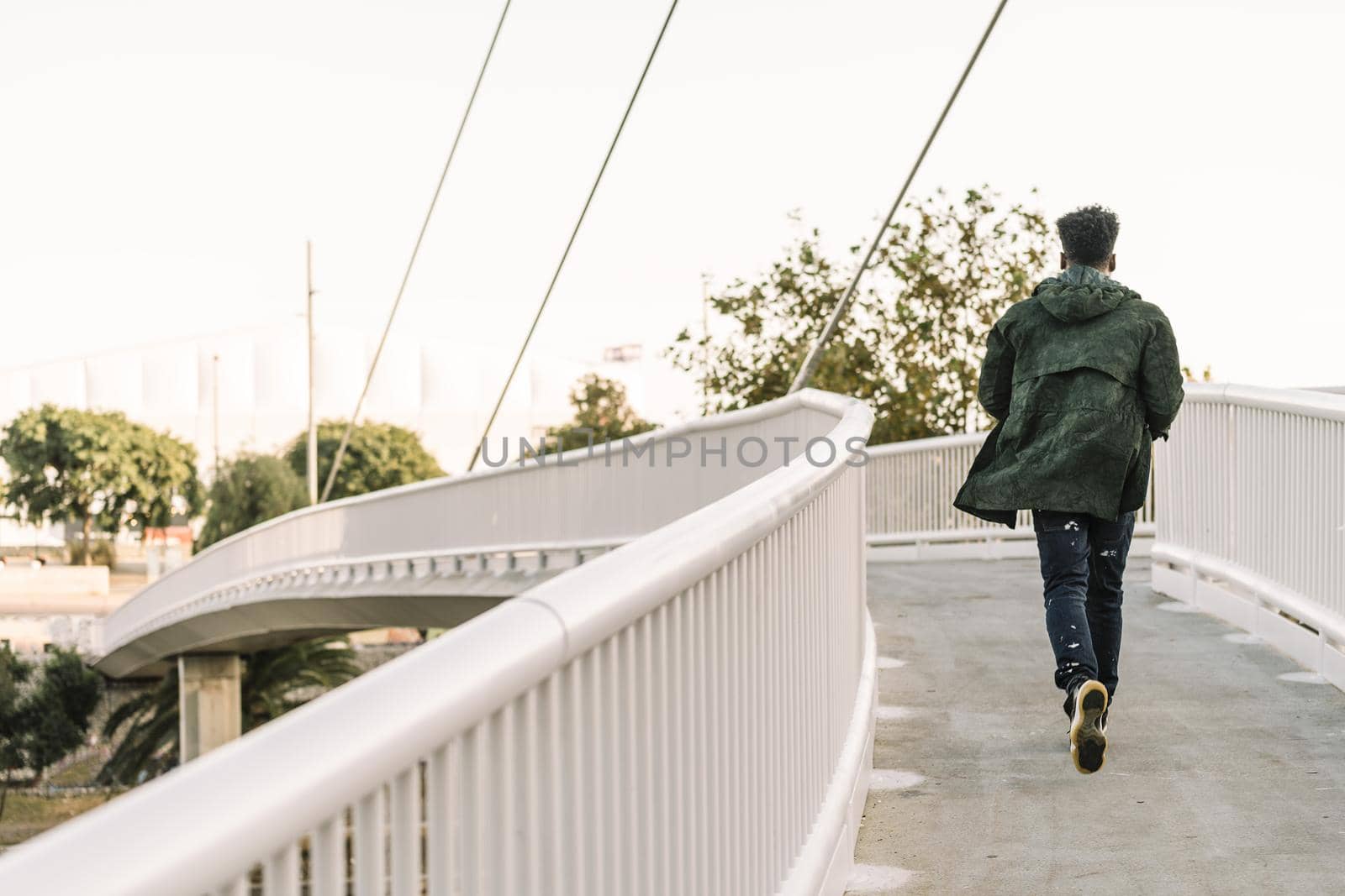 view from behind attractive young black african man with cool casual wear running on a modern bridge in the city, lifestyle concept