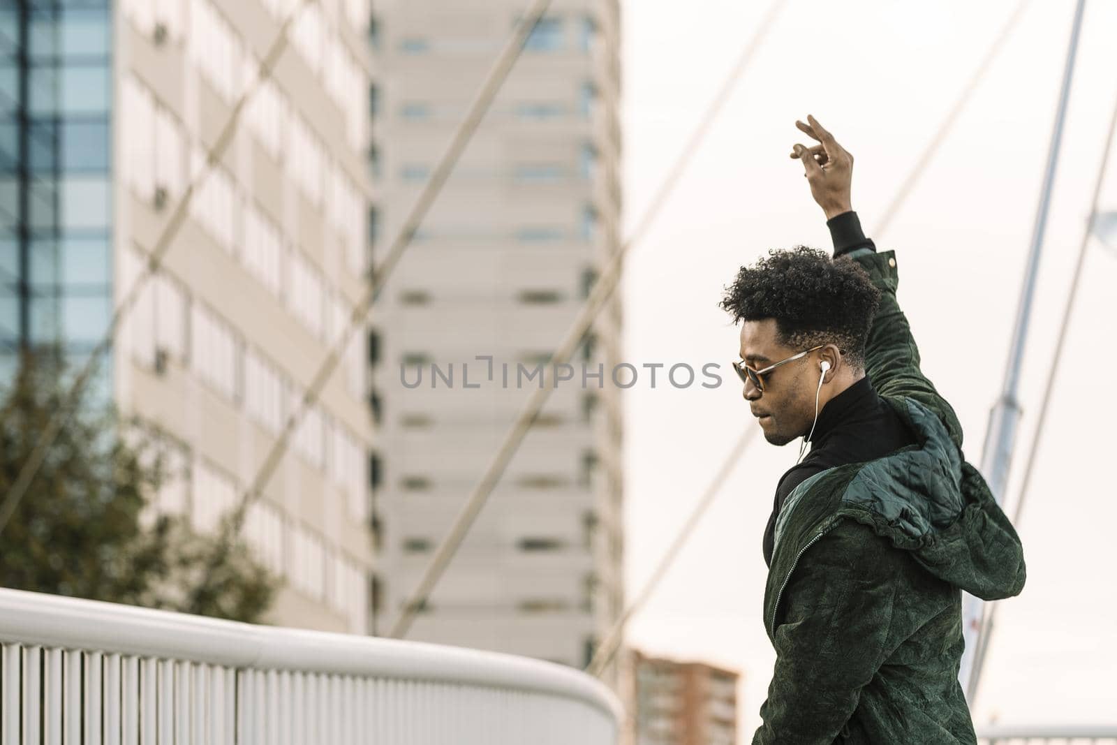 young attractive african black man with white earphones and sun glasses walking outdoor in the city having some fun and dancing, lifestyle and technology concept, copy space for text