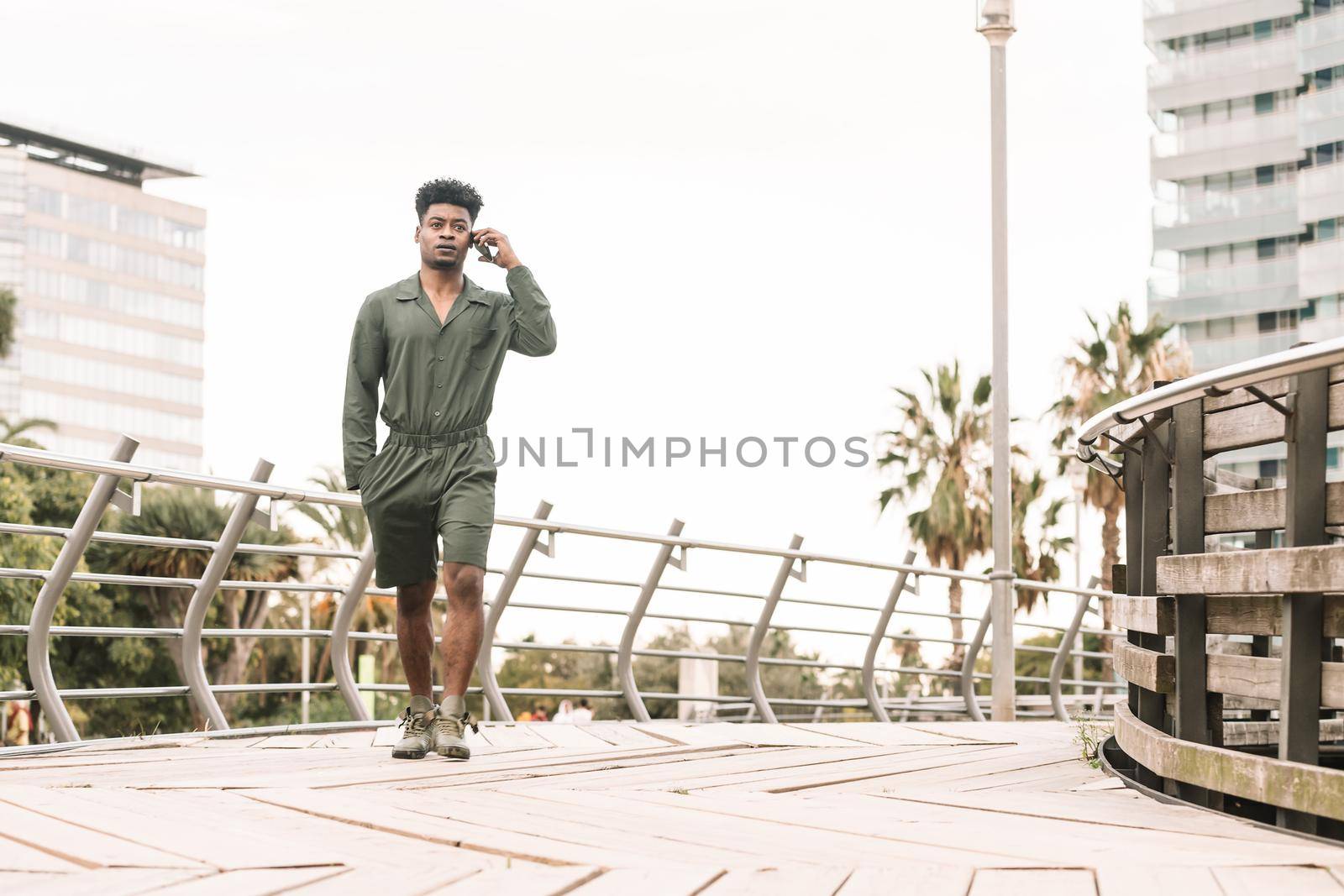 cool young african black man calling by phone while walks in a park outdoors in the city, lifestyle and technology concept, copy space for text