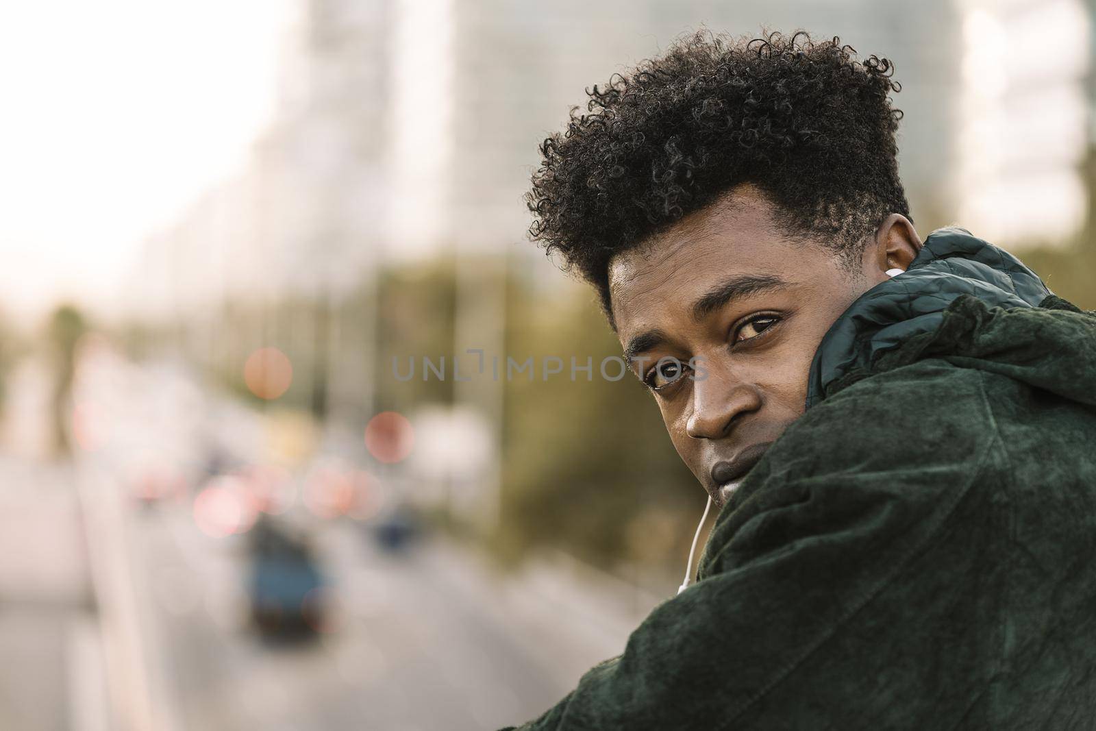 attractive young black african man with green jacket listening music with white earphones, city lifestyle concept