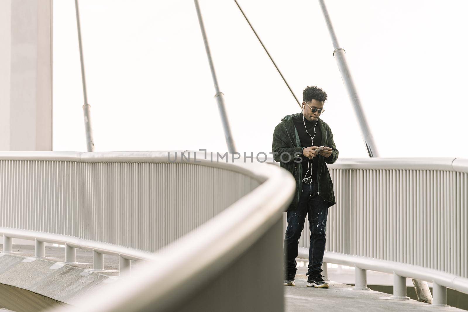 black man walks around looking at his smartphone while listen music in earphones in the city, technology and lifestyle concept using internet electronic device