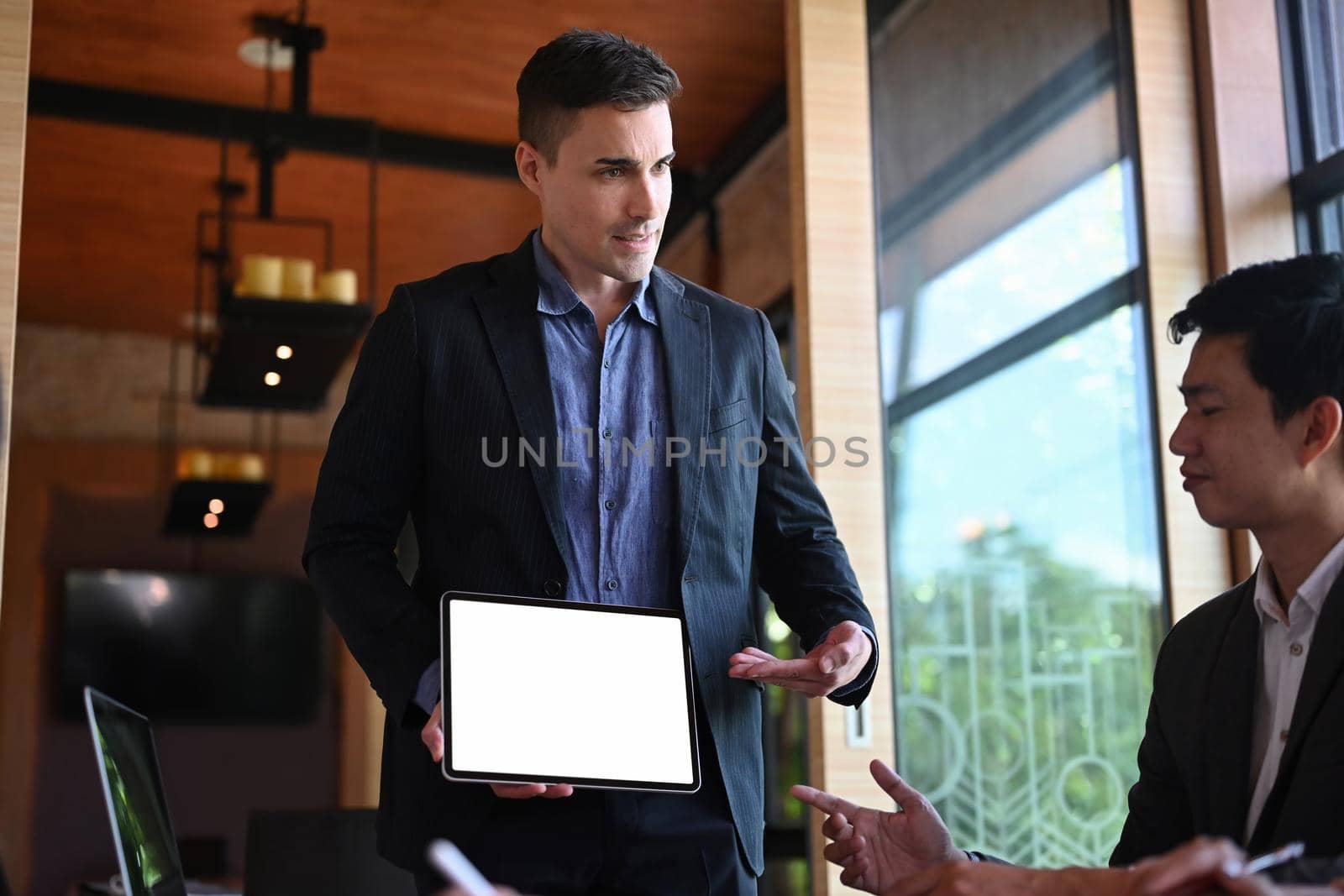 Confident executive businessman holding digital tablet and presentation financial information in modern conference room.