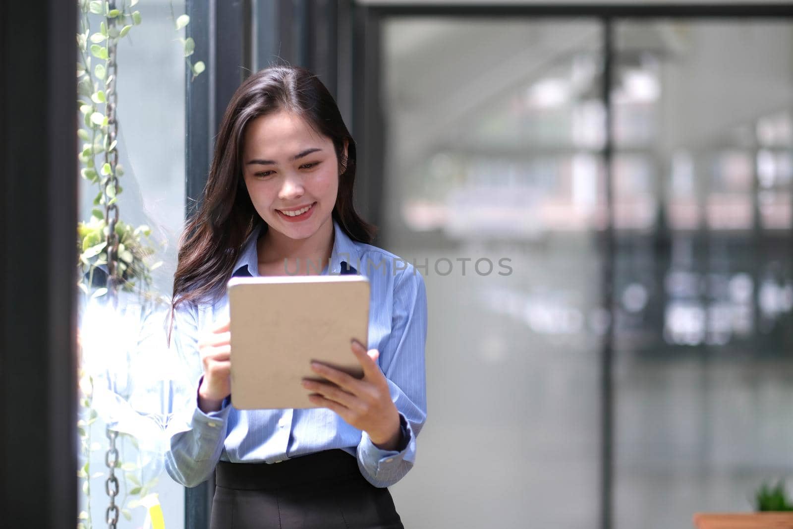 Beautiful businesswoman using stylus pen writing on tablet screen while standing in office room with copy space..