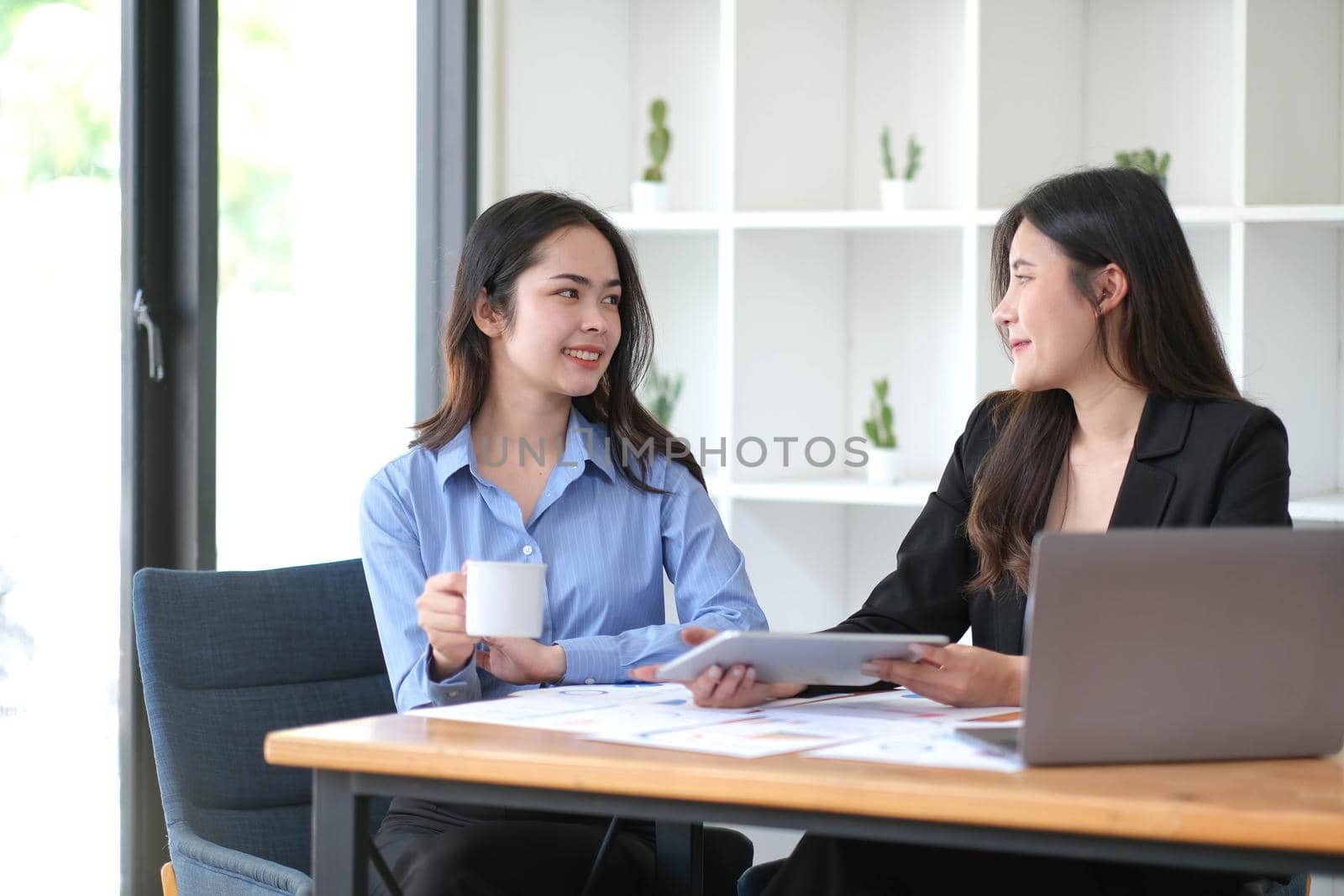 Two young Asian businesswoman discuss investment project working and planning strategy. Business people talking together with laptop computer at office. by wichayada