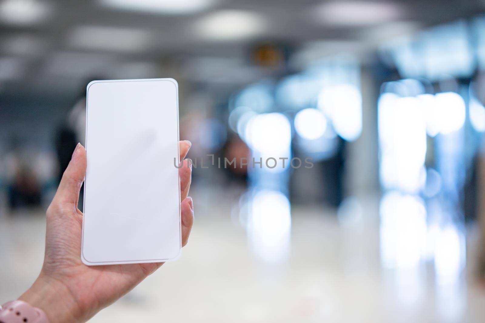 Hand holding smartphone with blank screen white Isolated on blur airport background. by sirawit99