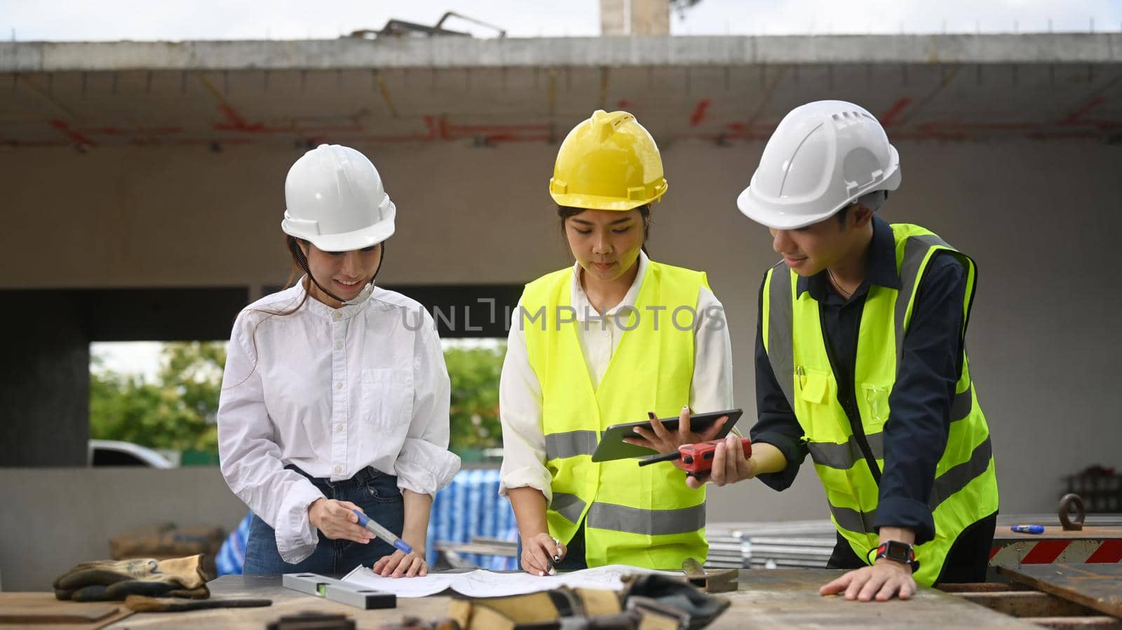 Architect team in safety helmet using digital tablet and working with blueprints during inspecting construction site by prathanchorruangsak