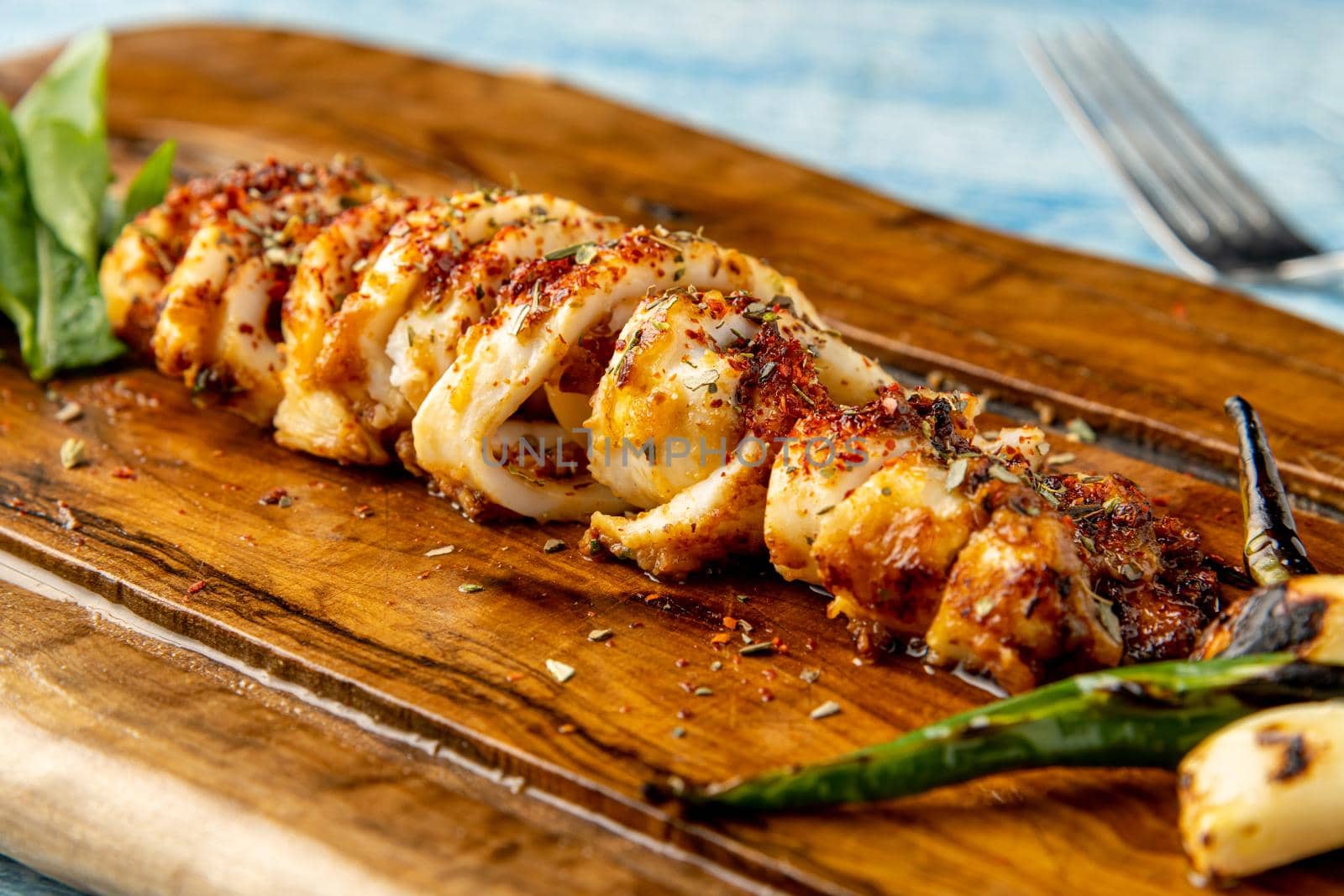 Spicy sliced grilled squid with green pepper and garlic on a wooden serving board by Sonat