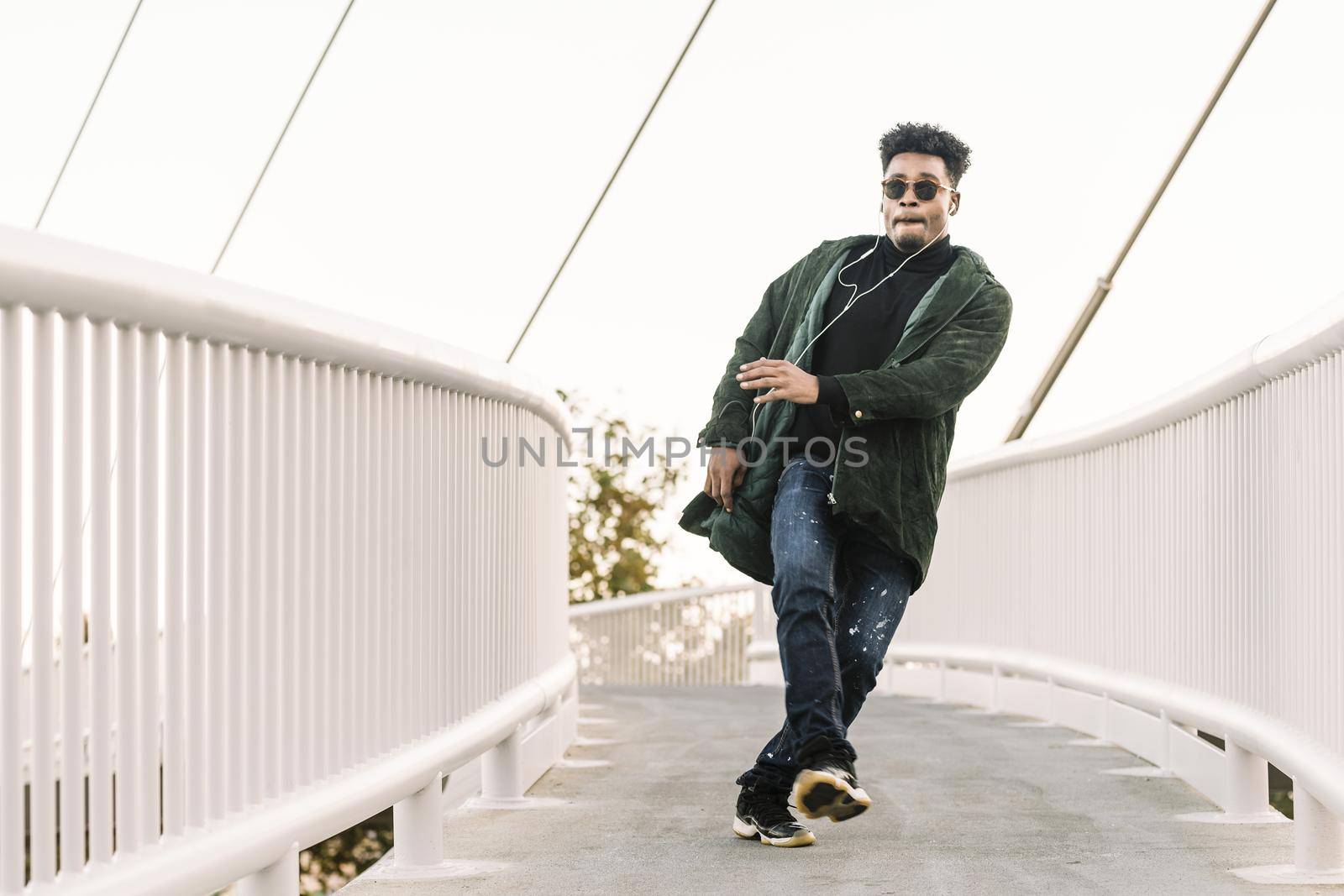 young stylish black guy with white earphones and sun glasses walking outdoor in the city, dancing happy and having some fun, lifestyle and technology concept, copy space for text