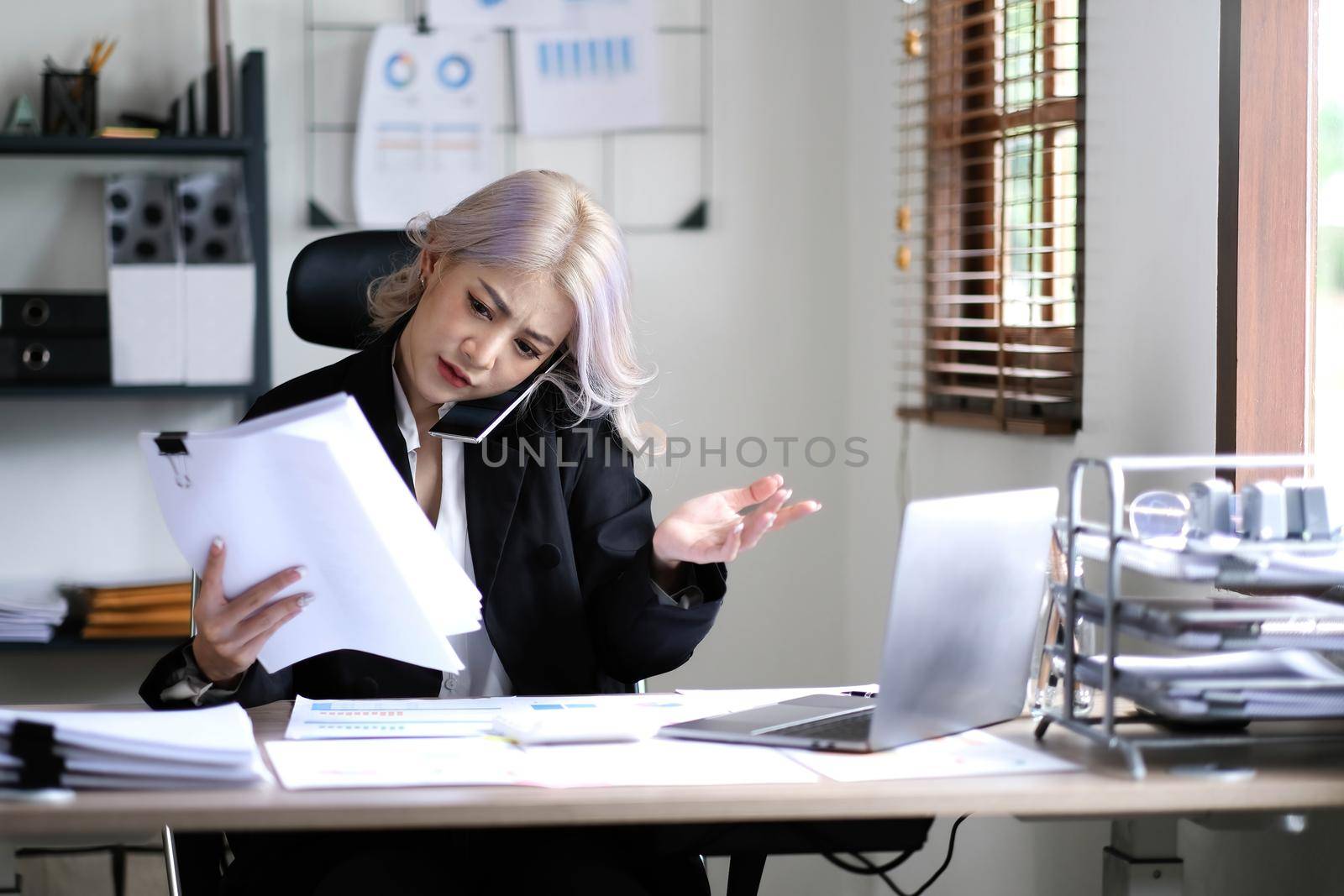 Asian woman cover her face with hand and feel upset while talk on mobile phone with customer in front of laptop computer on desk at office,Stress office lifestyle concept..
