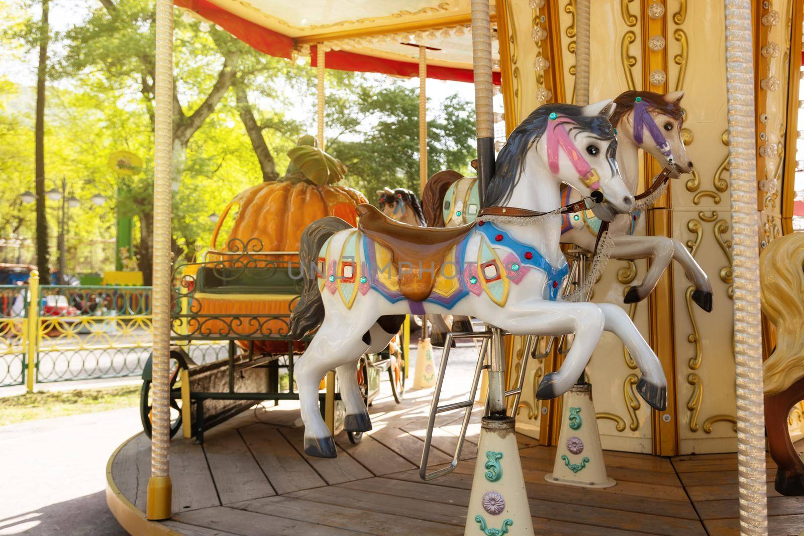 close-up of a colorful, beautiful carousel with horses and a carriage in an amusement park. Green park in summer, on a sunny day, copy space for your design
