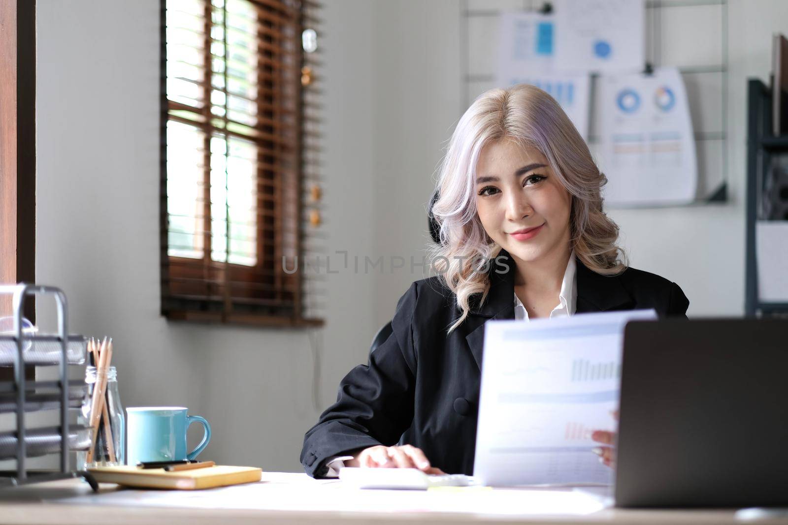 Beautiful Asian businesswoman analyzes charts using laptop calculator at the office..