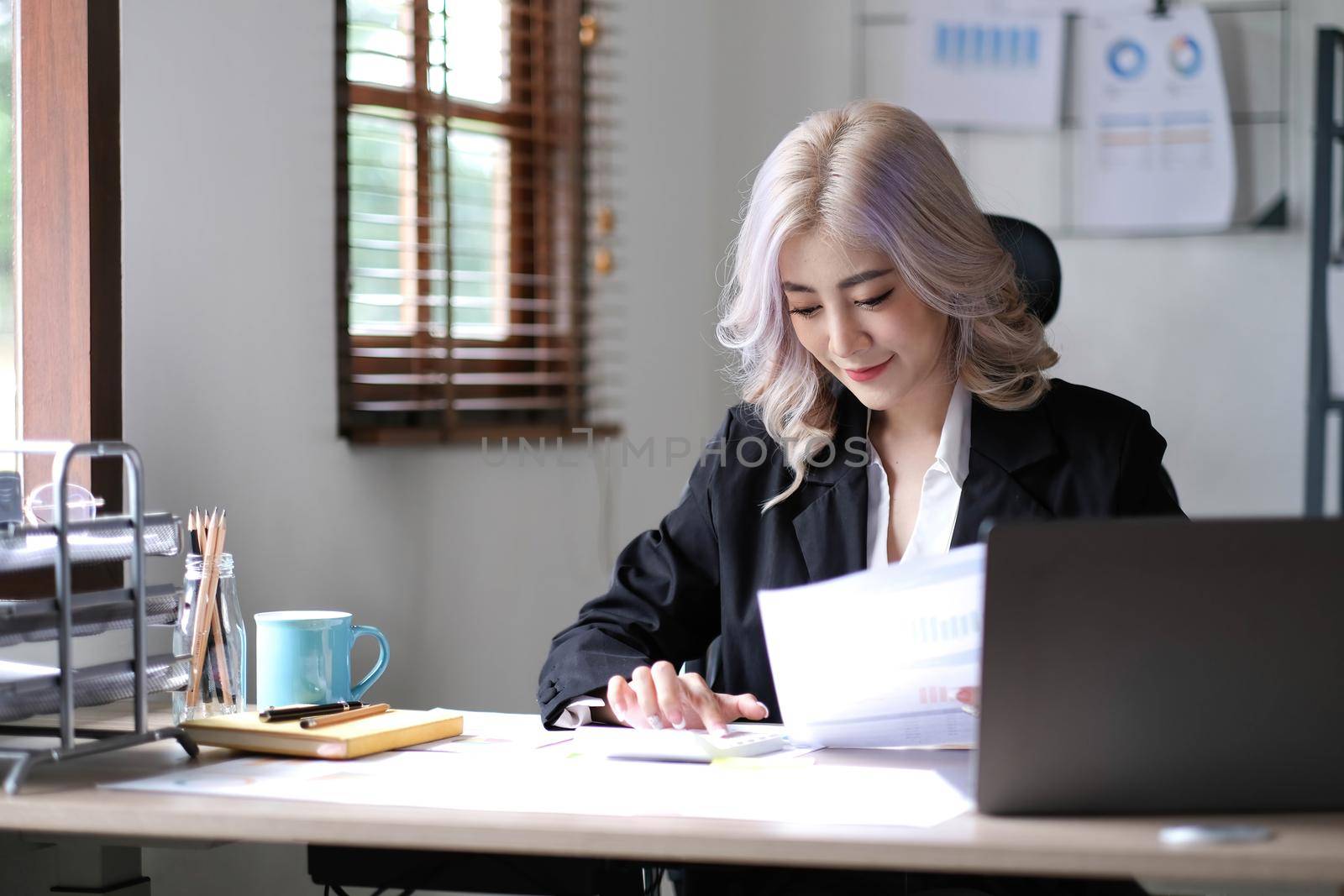 Beautiful Asian businesswoman analyzes charts using laptop calculator at the office..