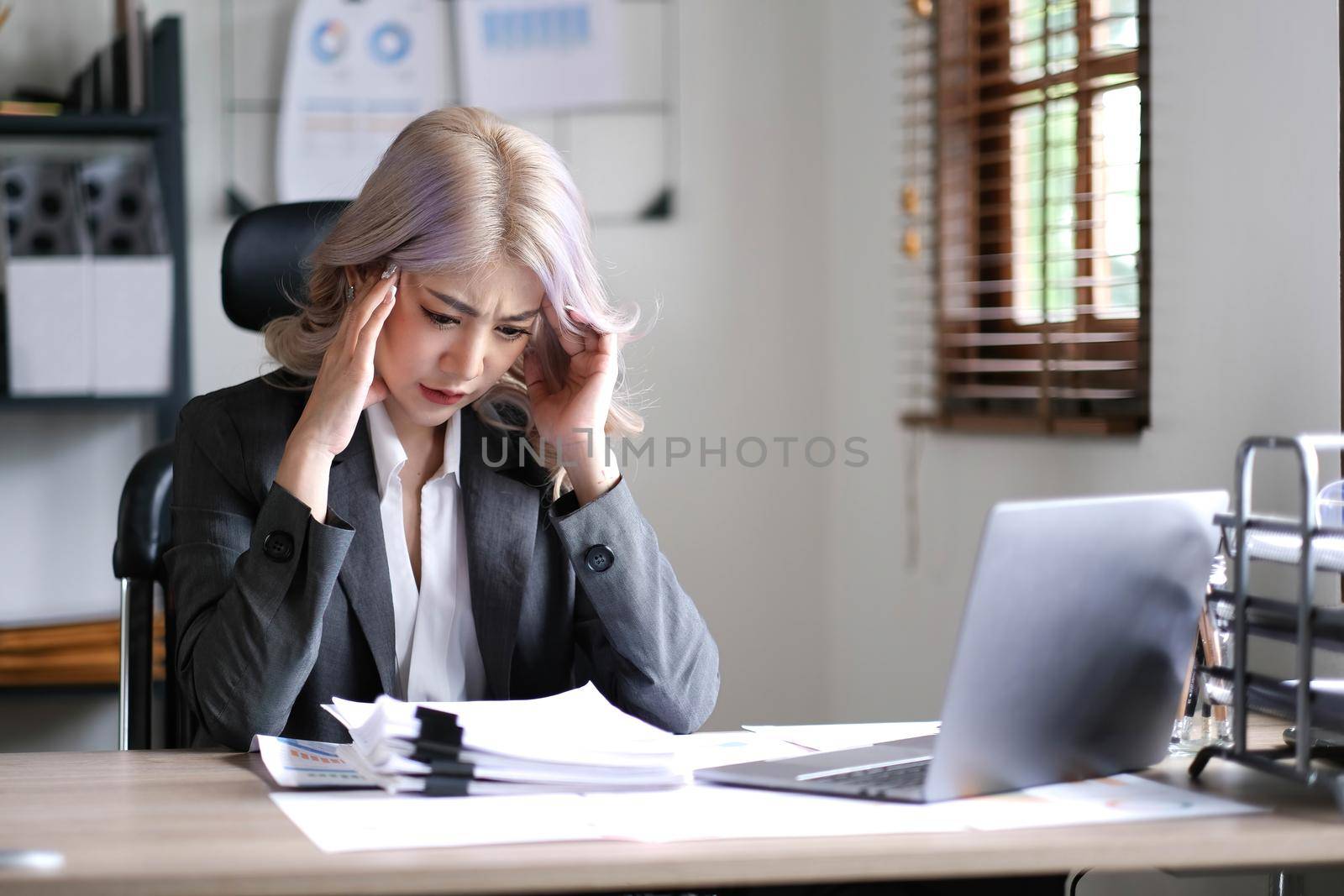 Asian businesswoman are serious at work causing headache stressed out with documents with a laptop at the office..