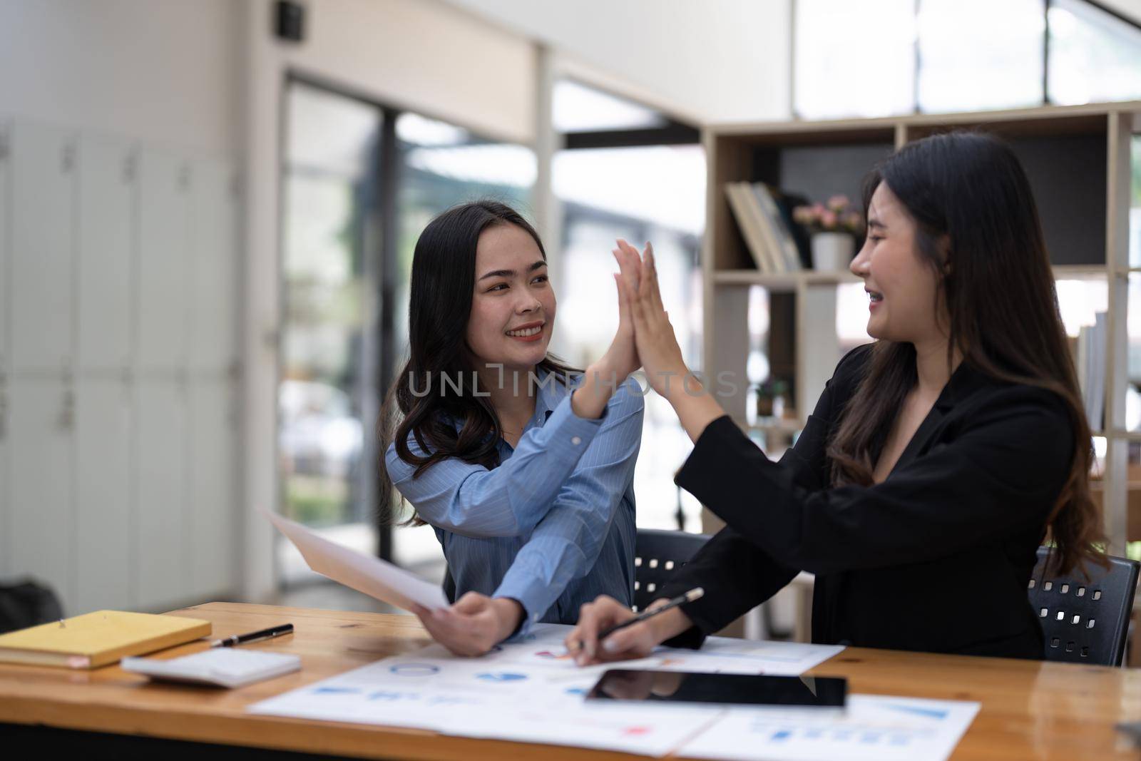 Two people hi five together for thier successful business project in meeting room. Two of business people looking at each other.