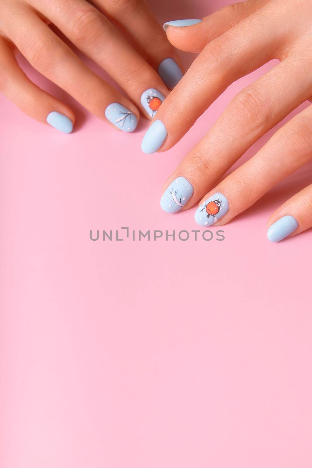 Female hands with winter snow manicure with stickers under a matte top on pink background.