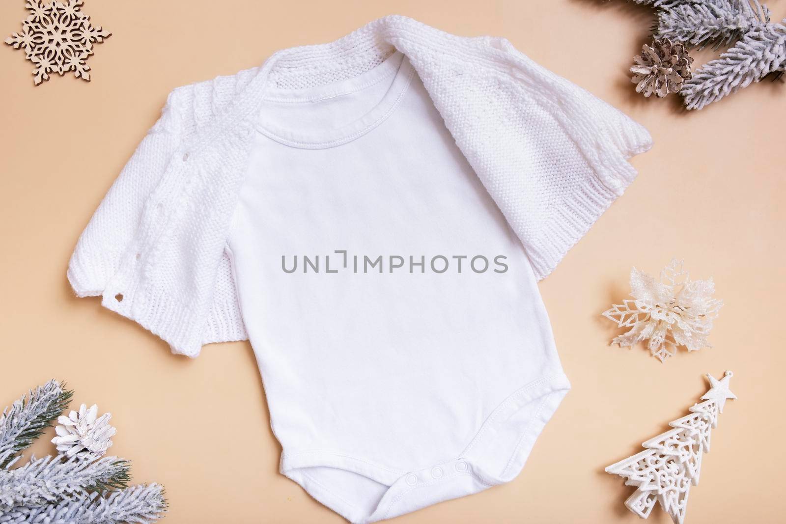 White baby bodysuit with sweater mockup for logo, text or design on beige background with winter decotations top view by ssvimaliss