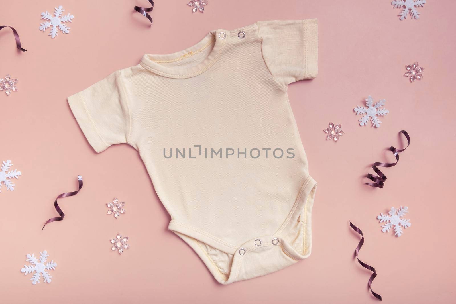 Yellow baby bodysuit mockup for logo, text or design on pink background with winter decotations top view by ssvimaliss