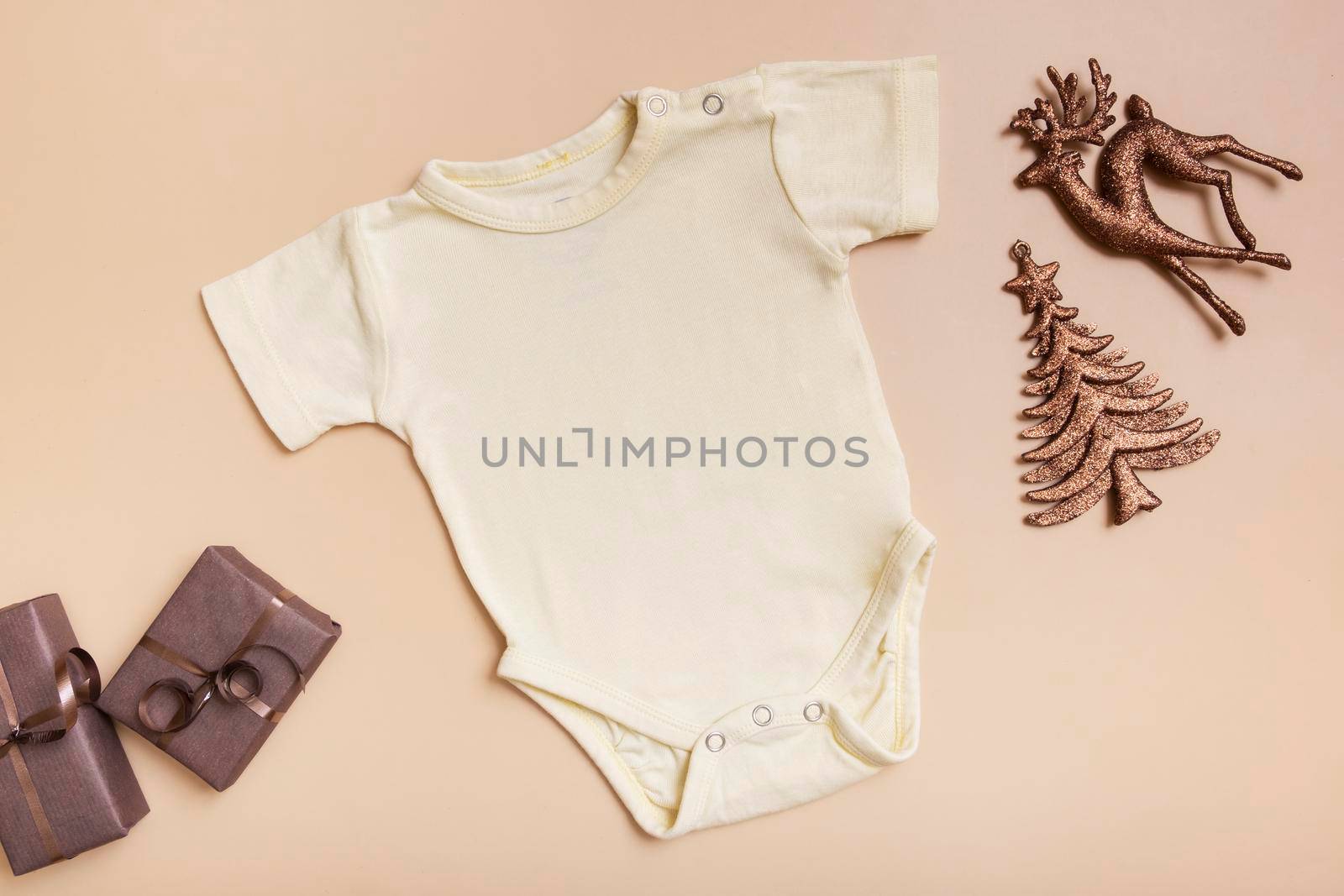 Yellow baby bodysuit mockup for logo, text or design on beige background with winter decotations top view.