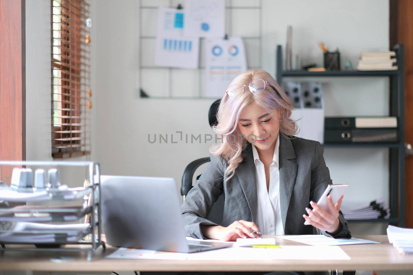 Happy young Asian business woman with a smile using smartphone at the office..
