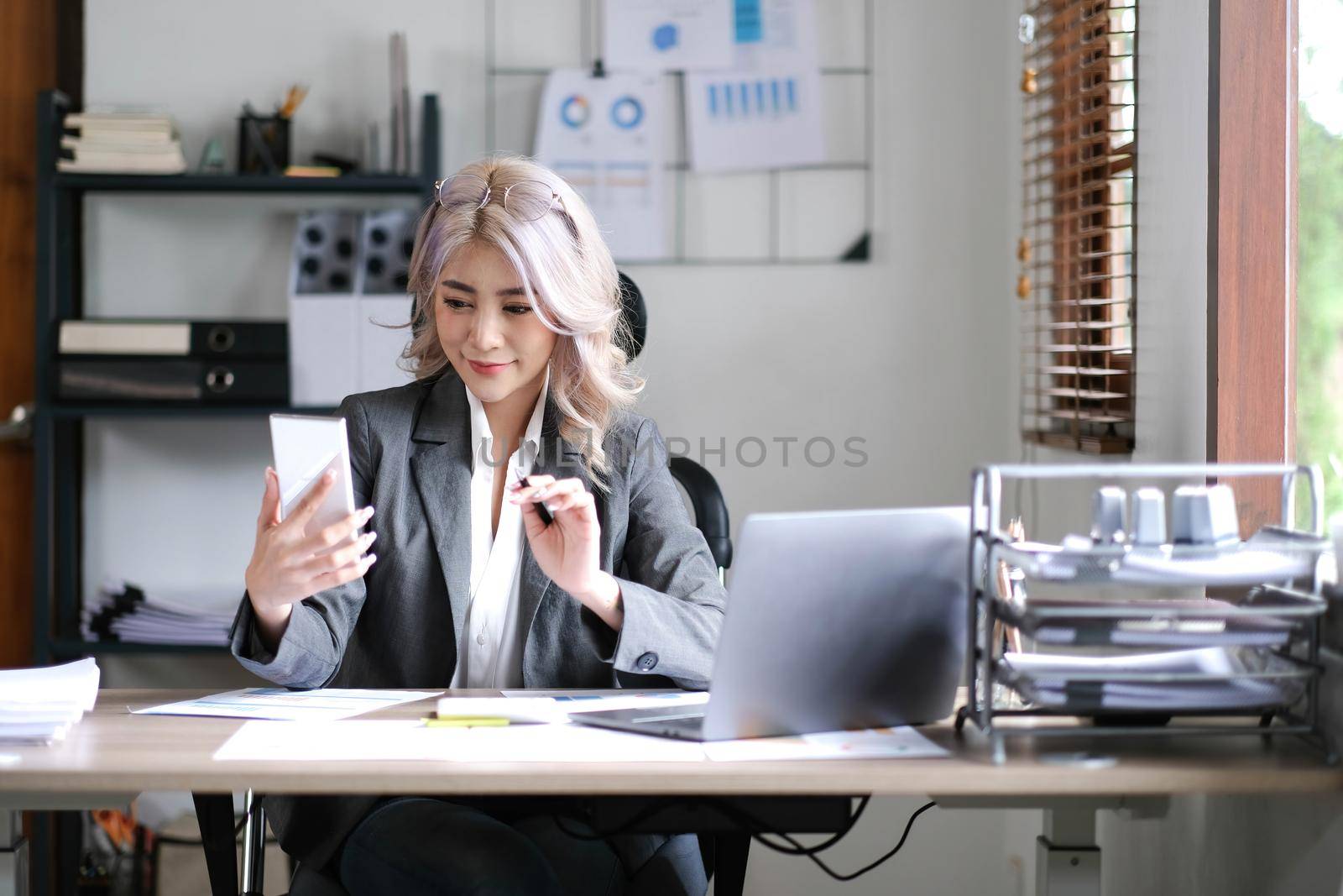 Happy young Asian business woman with a smile using smartphone at the office..