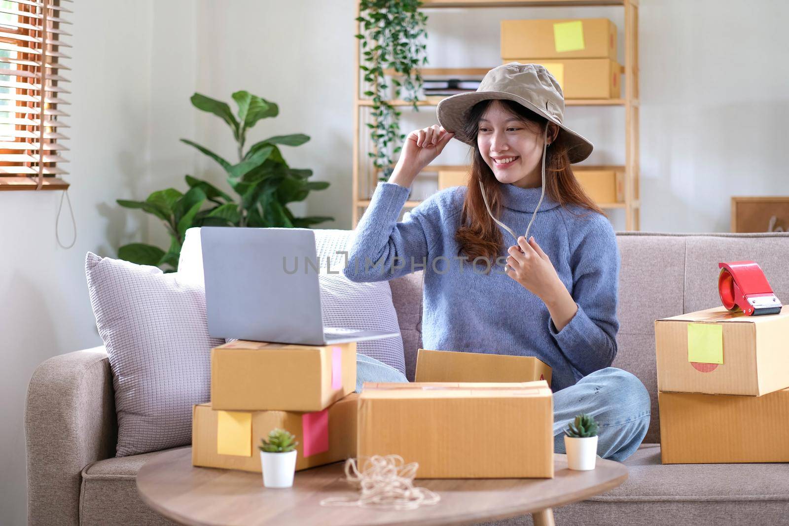 Startup small business entrepreneur SME, asian woman packing hat in box. Portrait young Asian small business owner home office, online sell marketing delivery, SME e-commerce telemarketing concept.