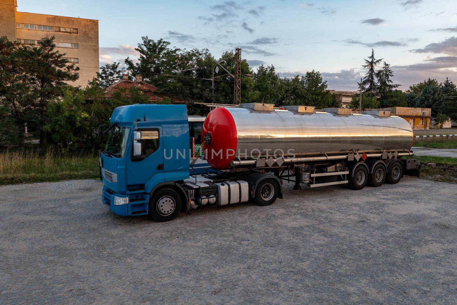 Big metal fuel tanker truck shipping fuel against a cloudy sky.
