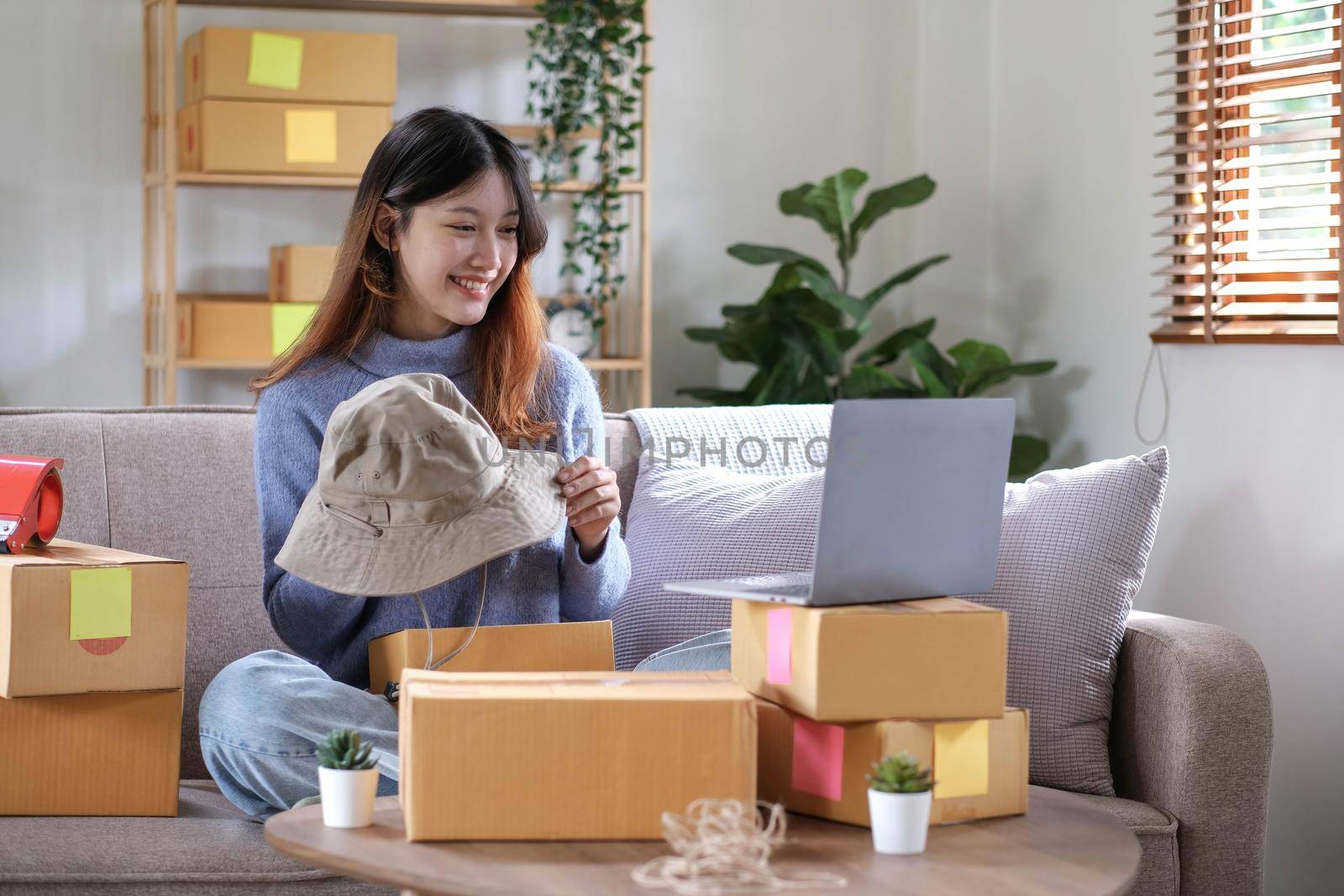 Startup small business entrepreneur SME, asian woman packing hat in box. Portrait young Asian small business owner home office, online sell marketing delivery, SME e-commerce telemarketing concept.