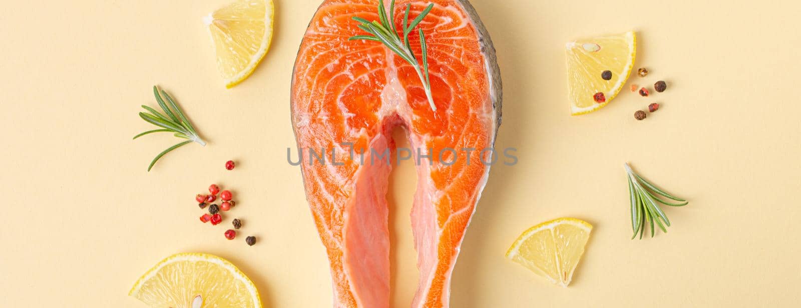 Uncooked raw fresh fish salmon steak top view on beige pastel background with rosemary, lemon wedges and spices, delicacy healthy fish cooking and nutrition concept flat lay