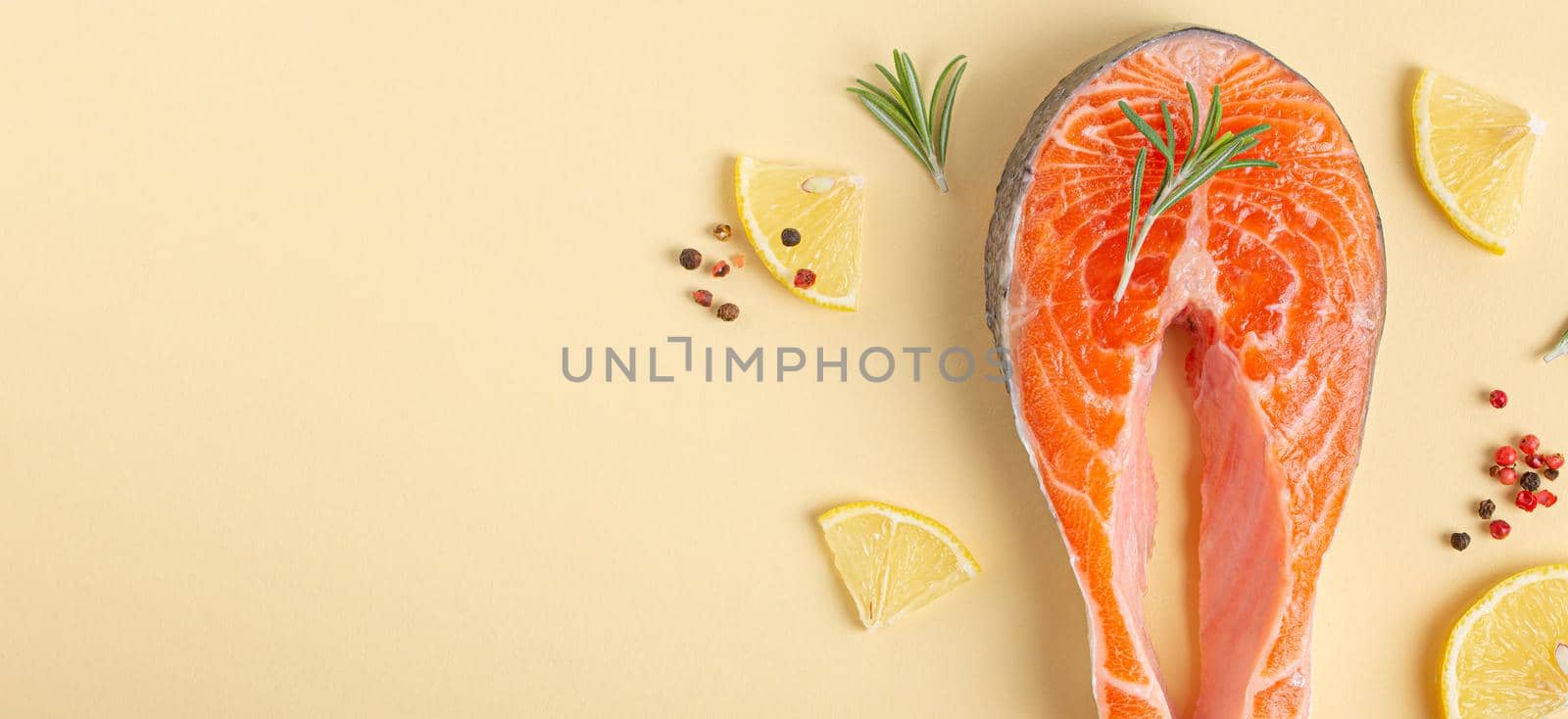 Uncooked raw fresh fish salmon steak top view on beige pastel background with rosemary, lemon wedges and spices, delicacy healthy fish cooking and nutrition concept flat lay space for text