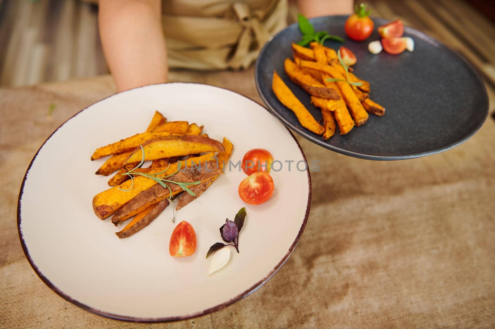 Top view plates with fried slices of organic batata or sweet potato wedges drizzled with olive oil in chef's hands by artgf