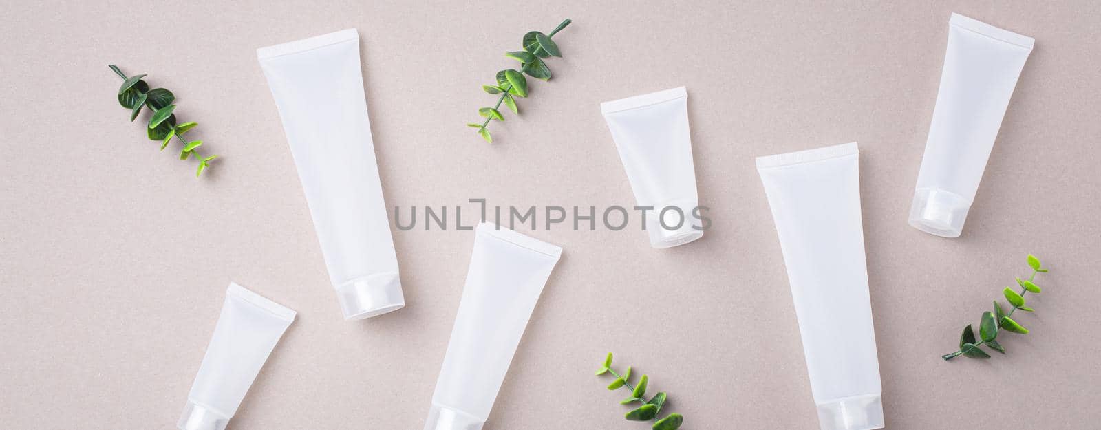 Set of skincare organic beauty product bottles and SPA cosmetic blank white matte containers with green plant leaves eucalyptus on gray clean background from above, flat lay mockup