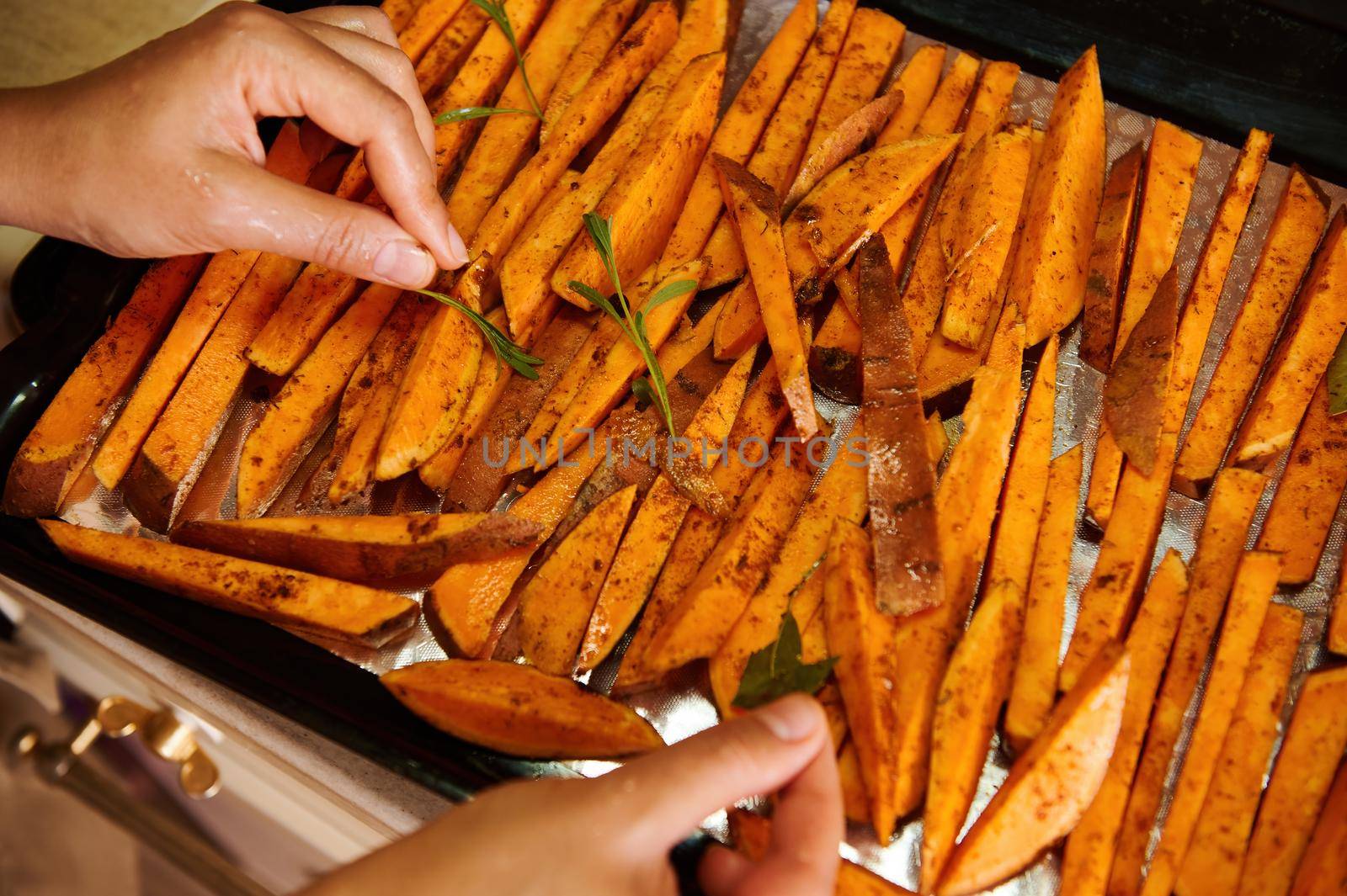 Healthy sweet potato fries on a baking sheet. Delicious vegan meal - roasted batata wedges baked with rosemary leaves by artgf