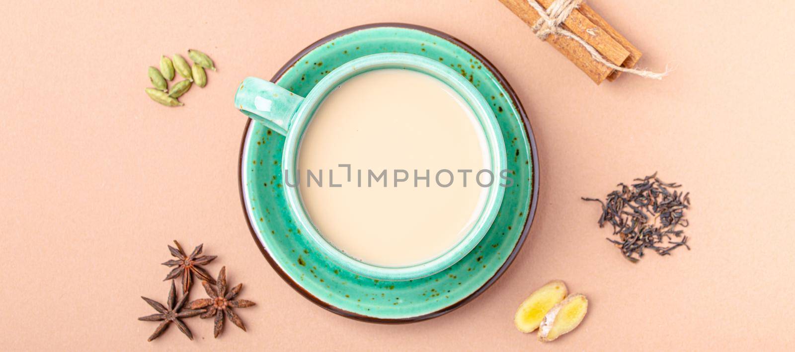 Healthy Indian beverage masala chai - tea hot drink with milk and spices in rustic green teacup with ingredients for making masala chai from above on simple beige minimal background