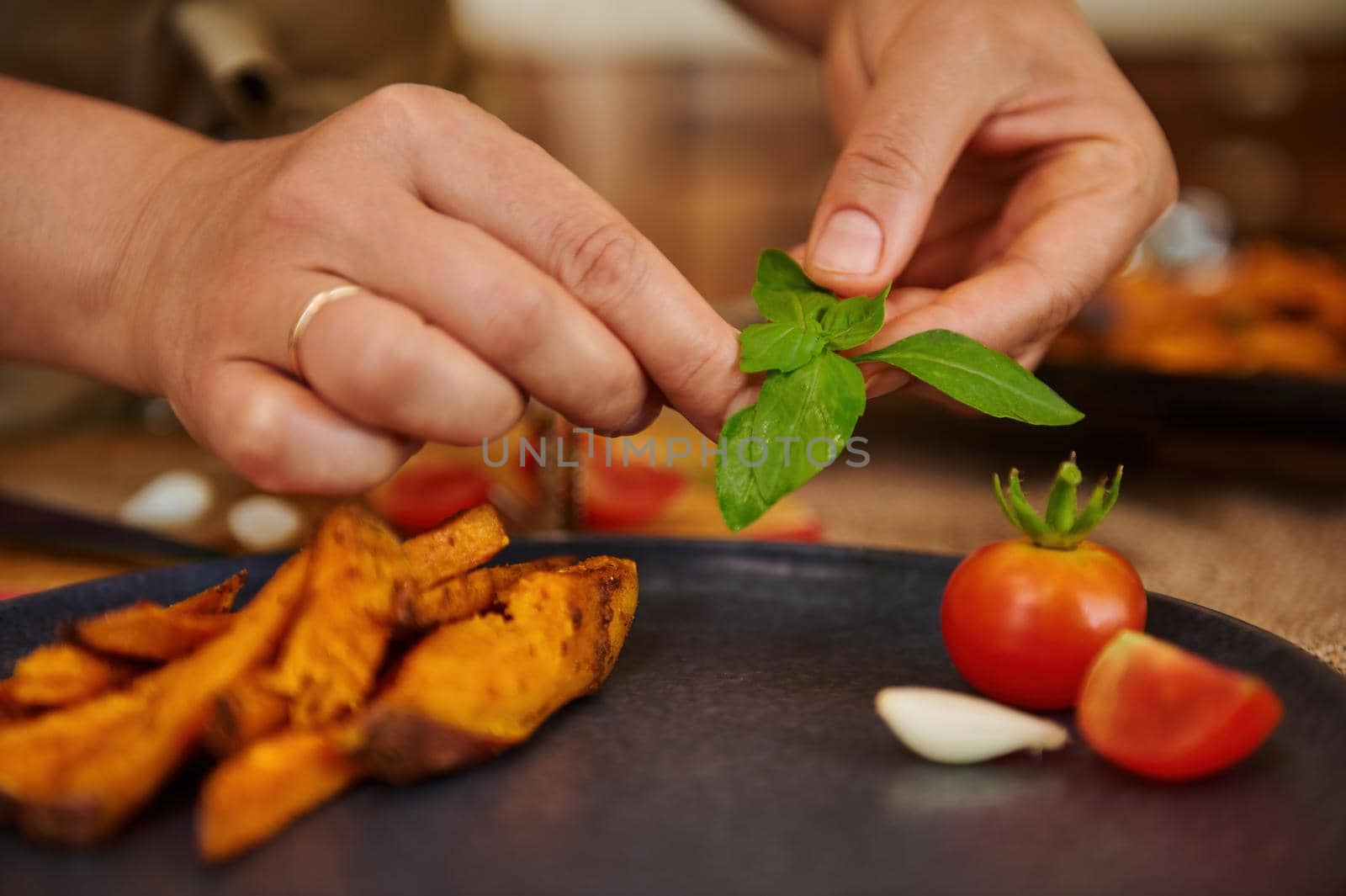 Chef's hands serving dish, putting basil leaf on the top of fried wedges of organic sweet potato. Healthy vegan meal by artgf