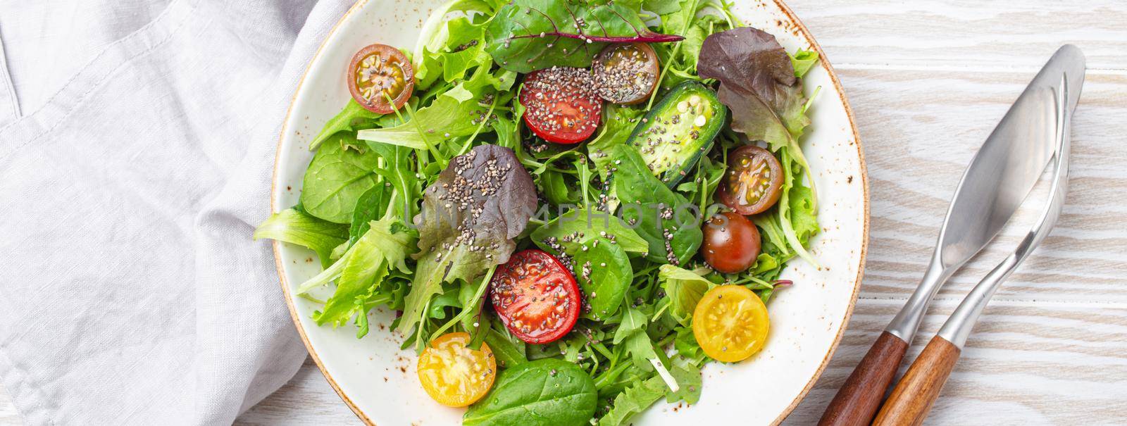 Vegetables vegetarian healthy salad with red yellow cherry tomatoes, green leafs and chia seeds on white plate on white wooden rustic background top view, healthy food and diet concept