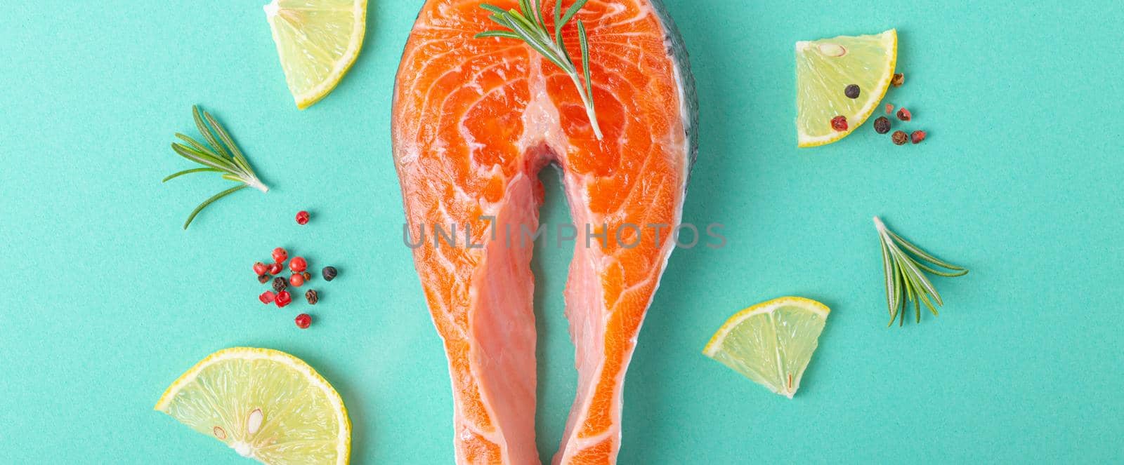 Uncooked raw fresh fish salmon steak top view on blue background with rosemary, lemon wedges and spices, delicacy healthy fish cooking and nutrition concept flat lay