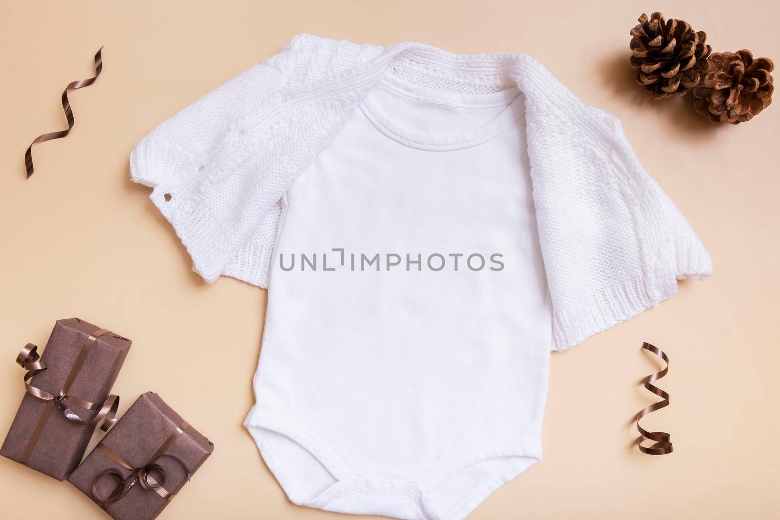 White baby bodysuit mockup for logo, text or design on beige background with winter decotations top view by ssvimaliss