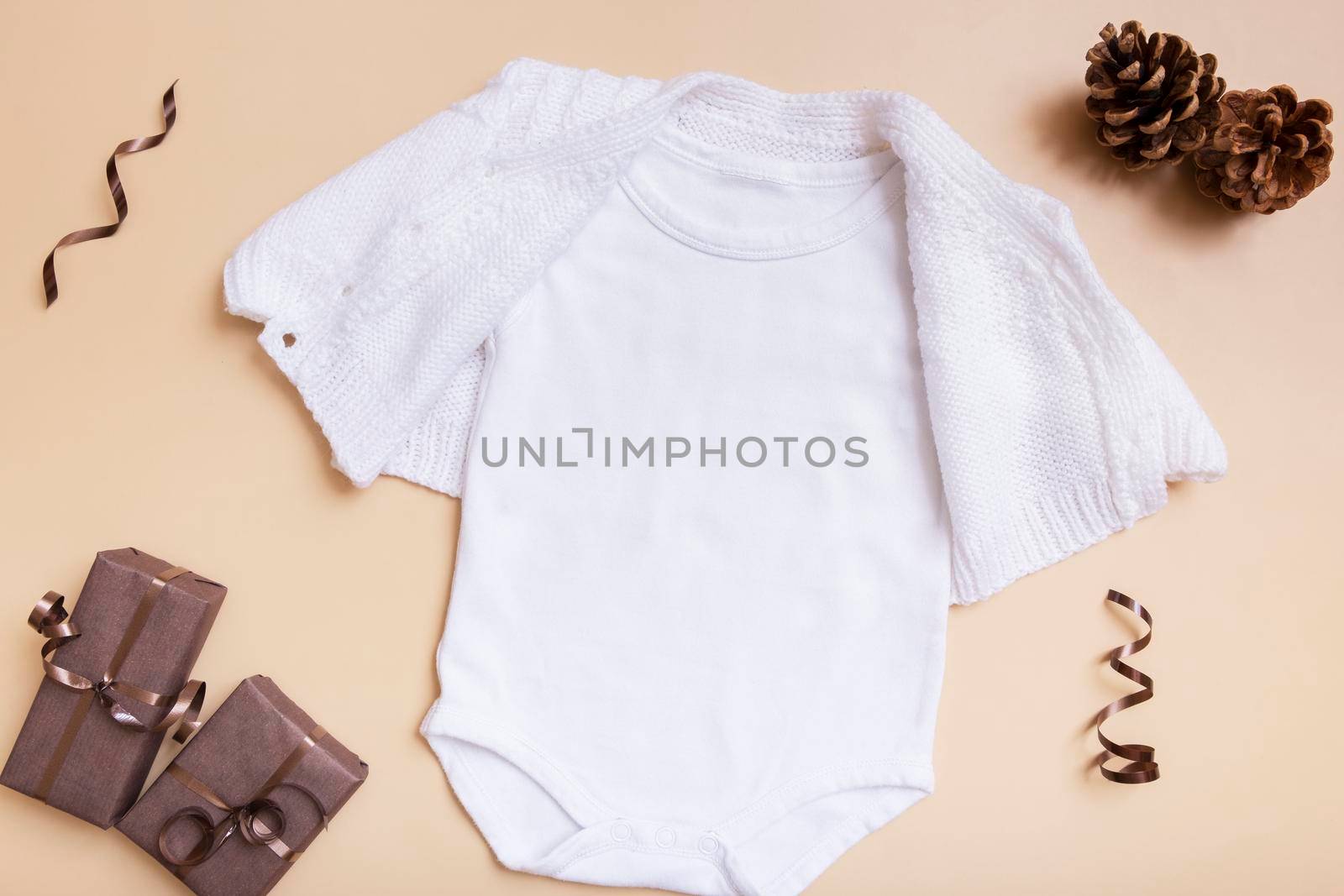 White baby bodysuit mockup for logo, text or design on beige background with winter decotations top view.