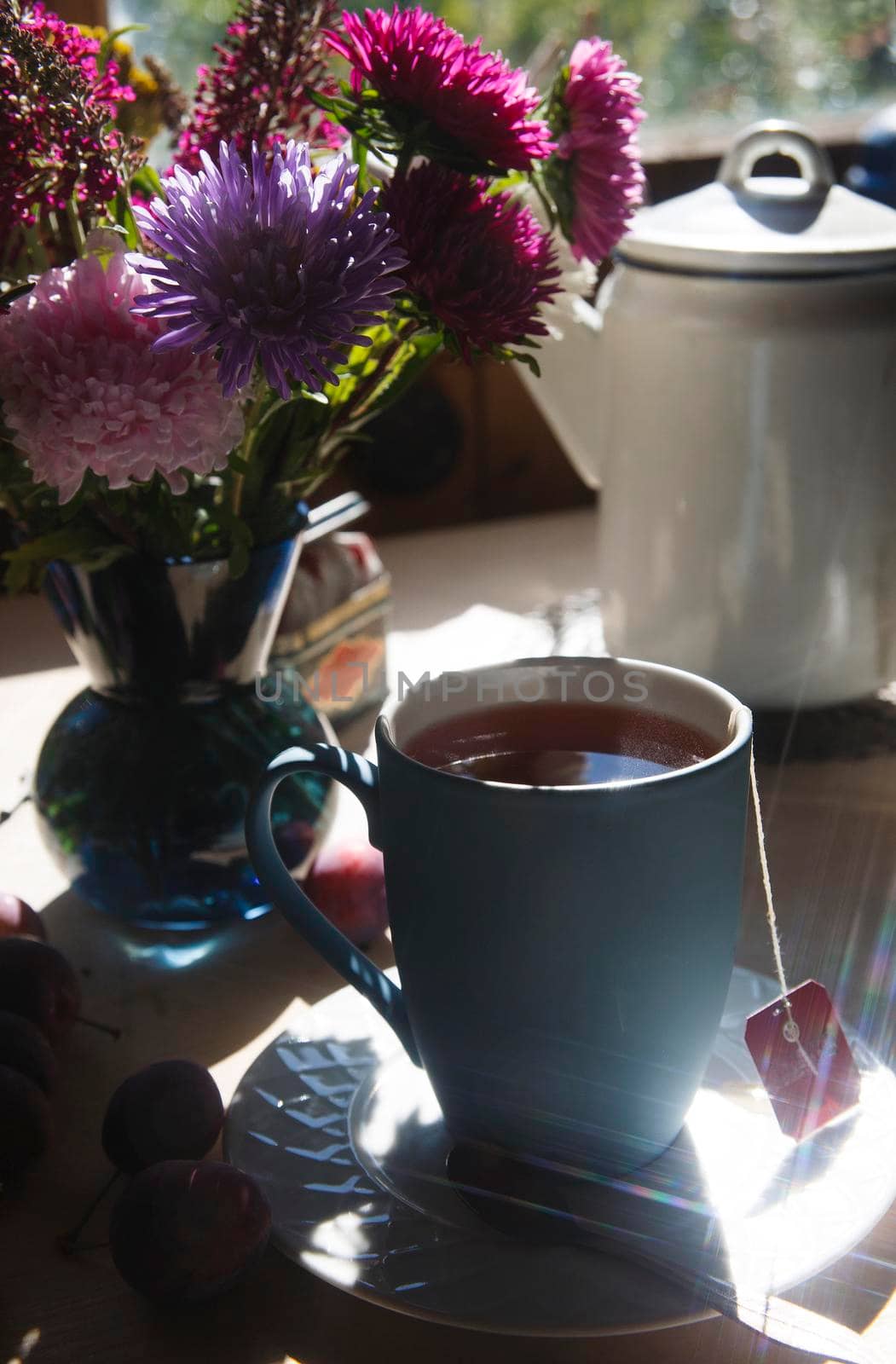 Blue cup of tea with bouquet of blue, pink and purple aster flowers in the bright light, morning tea concept, selective focus.