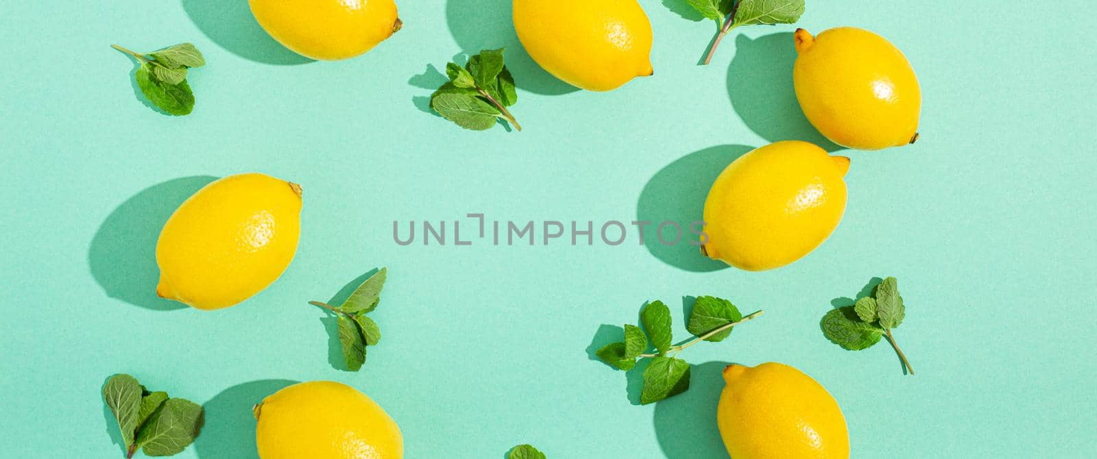 Fresh yellow lemons with mint on minimal blue background on bright sun light with hard shadows pattern summer background flat lay from above, citrus food composition, space for text